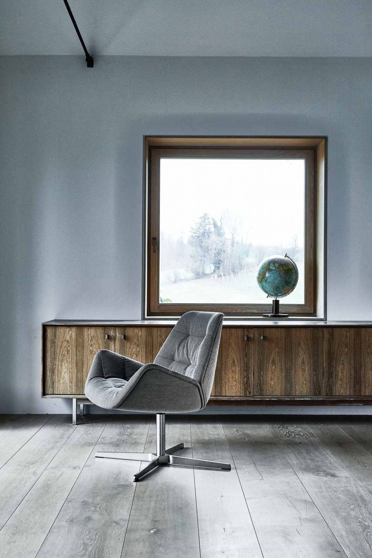 Moderner 809 Lounge Sessel von Thonet mit grauem Stoffbezug und silbernem Drehfuß vor Fenster.