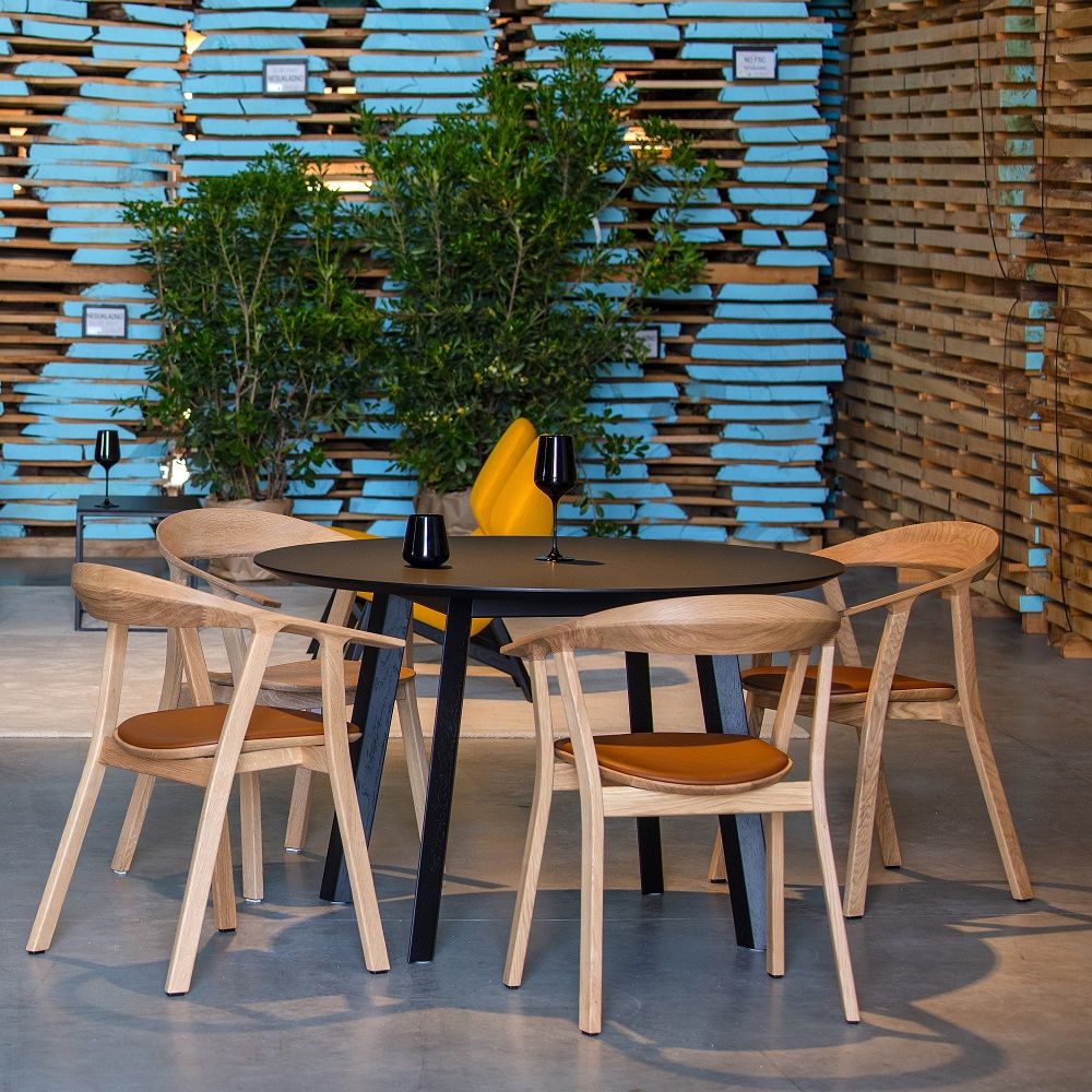 Rhomb Indoor Stuhl von Prostoria: Vier Holzstühle mit braunen Sitzflächen um einen runden, schwarzen Tisch.