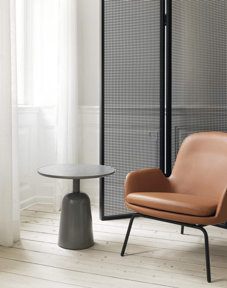 Grauer Normann Copenhagen Turn Table Tisch neben einem Sessel mit braunem Lederbezug auf hellem Holzboden.