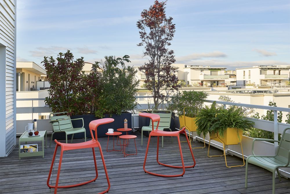 Adadesk Beistelltisch und Fermob Outdoor Möbel auf einer Dachterrasse mit Pflanzen und Stühlen.