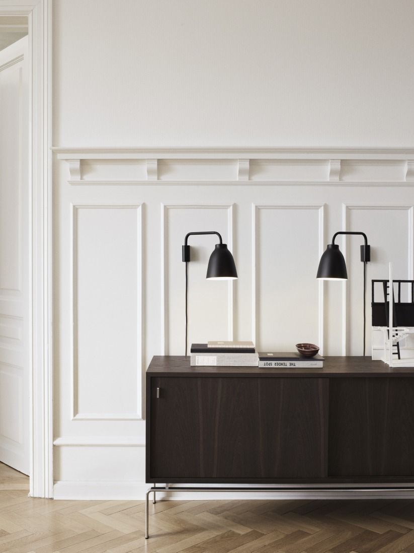 Zwei schwarze Caravaggio Read Wandleuchten von Fritz Hansen über einem Sideboard. Designleuchte für Wohnraum.