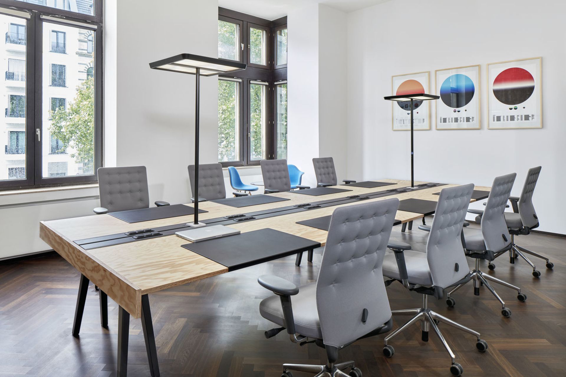 Konferenzraum mit langem Holztisch, Stehleuchten und mehreren grauen ID Trim Bürodrehstühlen von Vitra.