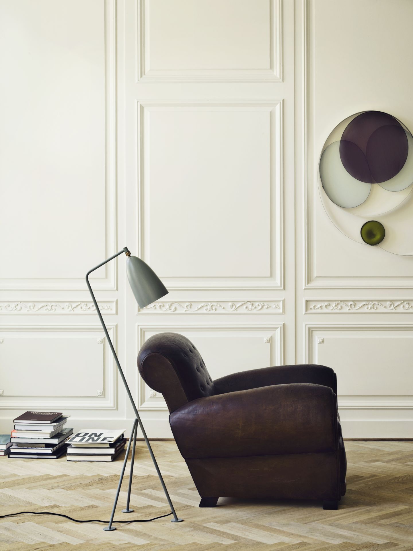 Gräshoppa Stehleuchte in Dusty Blue von Gubi neben Sessel und Bücherstapel im Interieur.