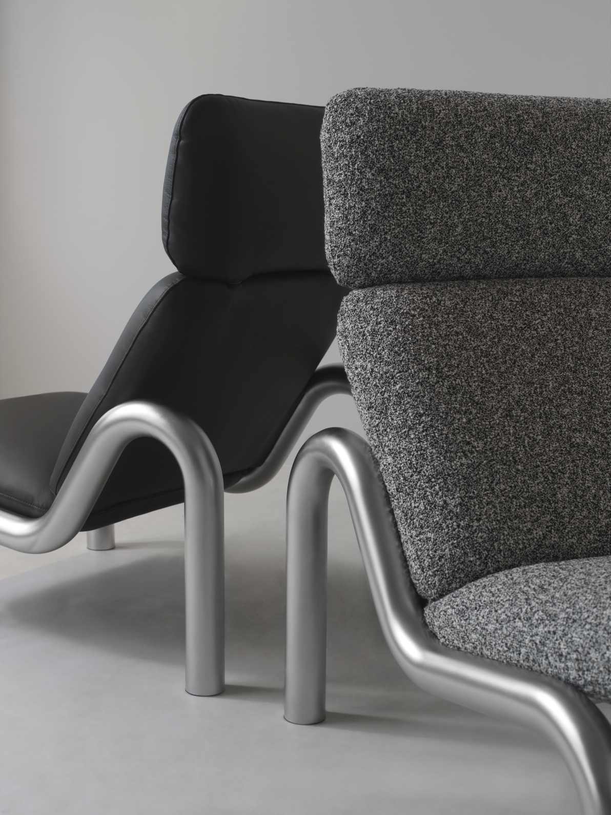 Nahaufnahme von zwei Tube Lounge Sesseln von Normann Copenhagen, einer in Schwarzleder, der andere in grauem Stoff.