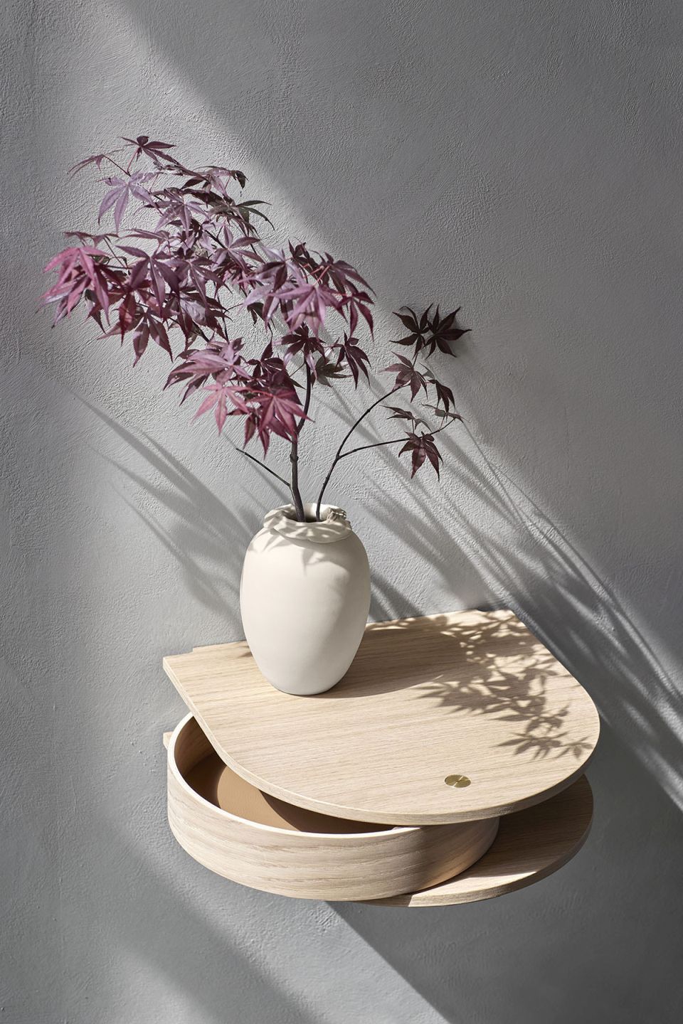 Northern Valet Wandschublade aus geräucherter Eiche mit geöffneter Schublade und Vase mit Zweigen an grauer Wand.