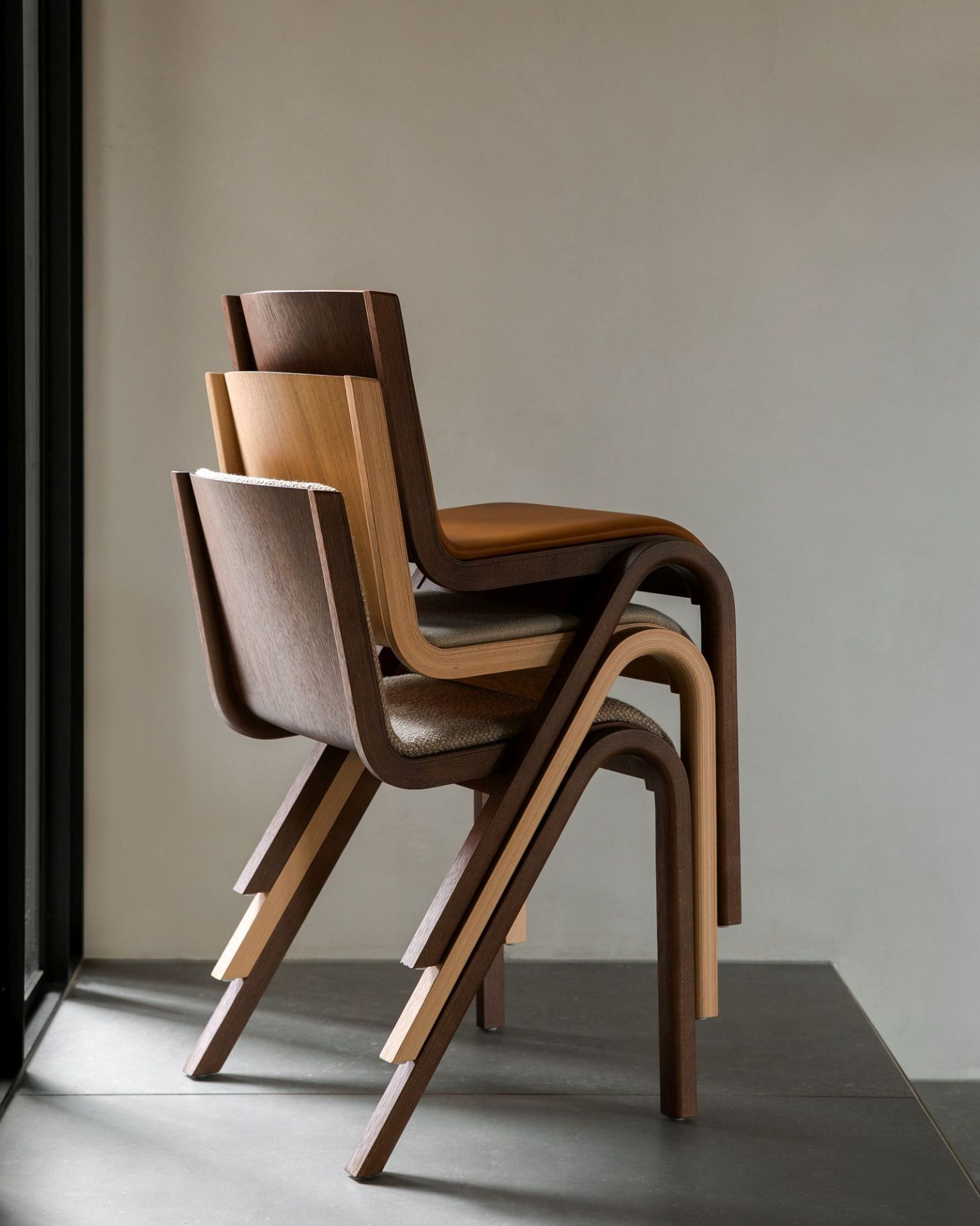 Stapel aus drei Audo Copenhagen Ready Dining Chairs mit Vollpolsterung in verschiedenen Holzfarben.