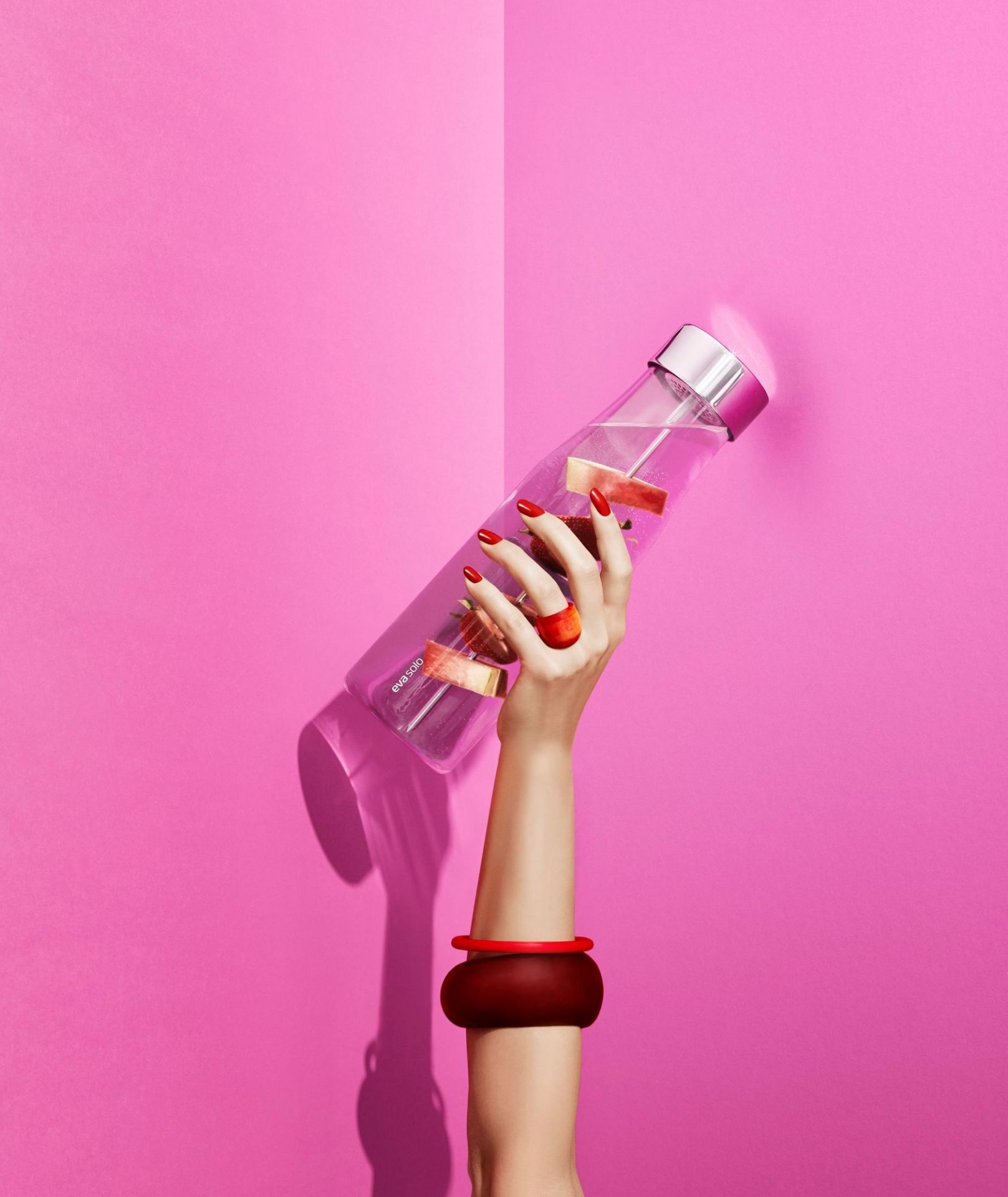 Frau hält Eva Solo My Flavour Karaffe mit Fruchtstücken vor pinkfarbenem Hintergrund. Stilvolle Wasserflasche für Infused Water.