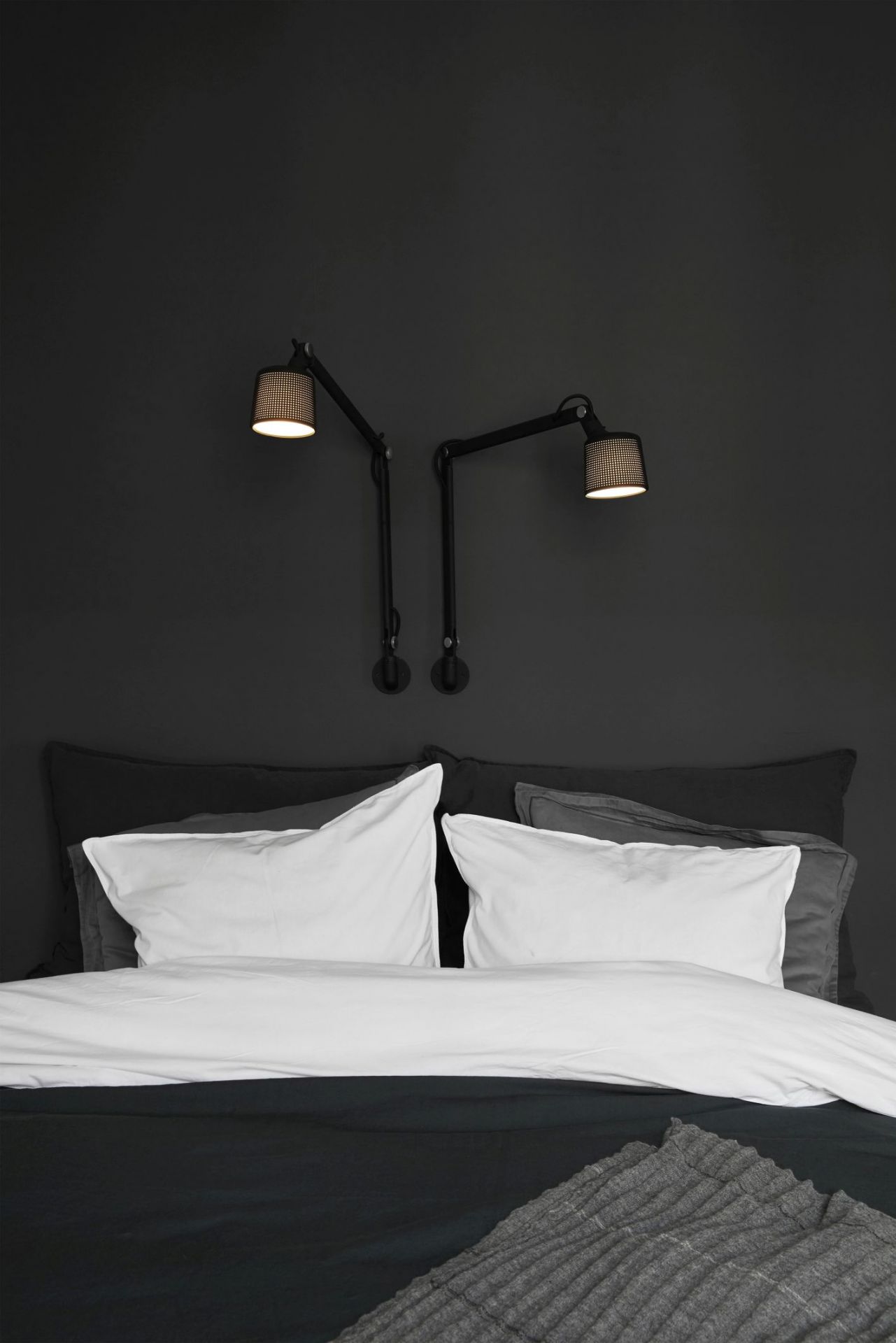Schlafzimmer mit Bett und zwei schwarzen Vipp Wandlampen als Nachttischlampen an der dunklen Wand.