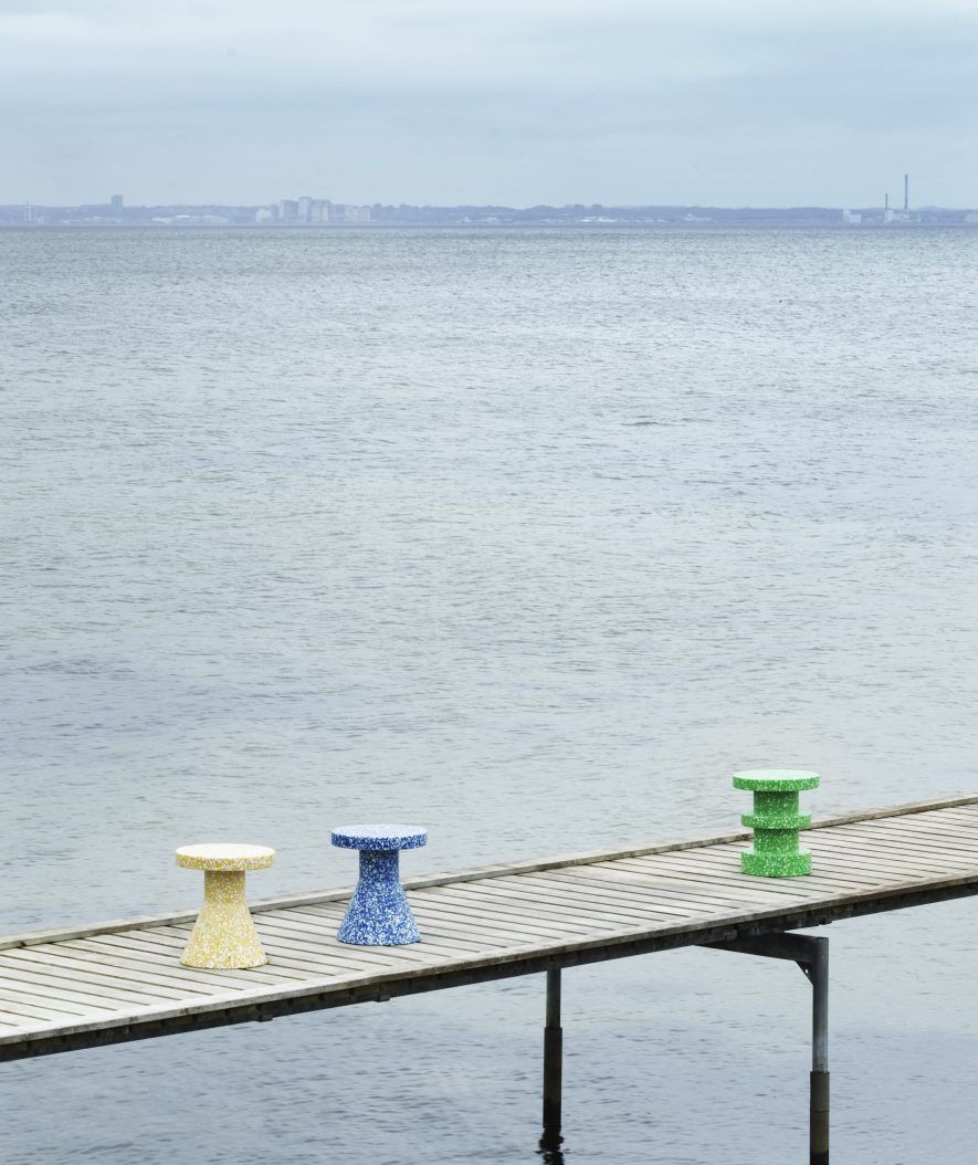Drei bunte Bit Stool Cone Hocker von Normann Copenhagen auf einem Holzsteg am Meer.
