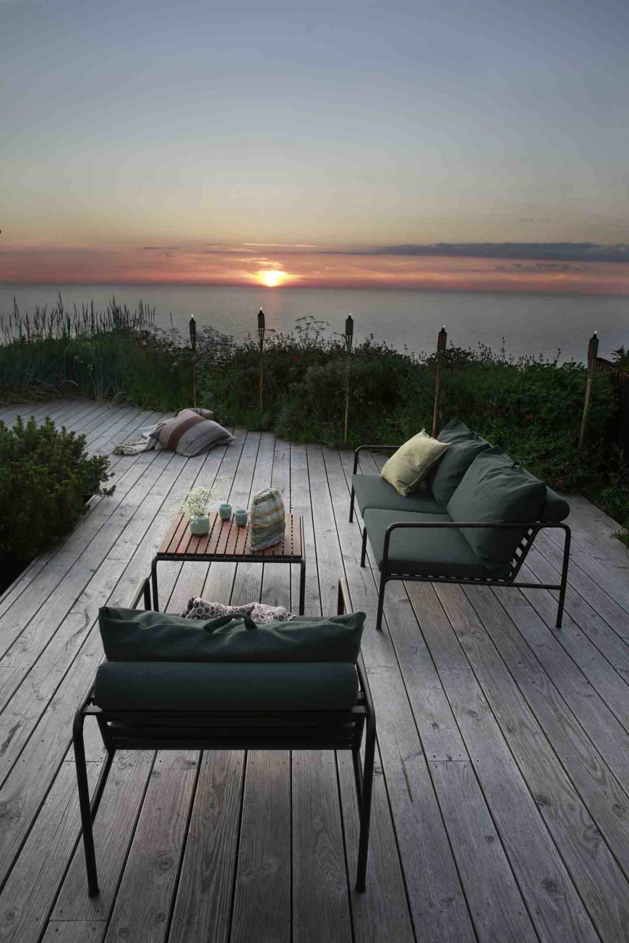 Avon 2-Sitzer Outdoor Sofa von Houe auf Holzterrasse mit Meerblick bei Sonnenuntergang. Gartenmöbel für entspannte Stunden.