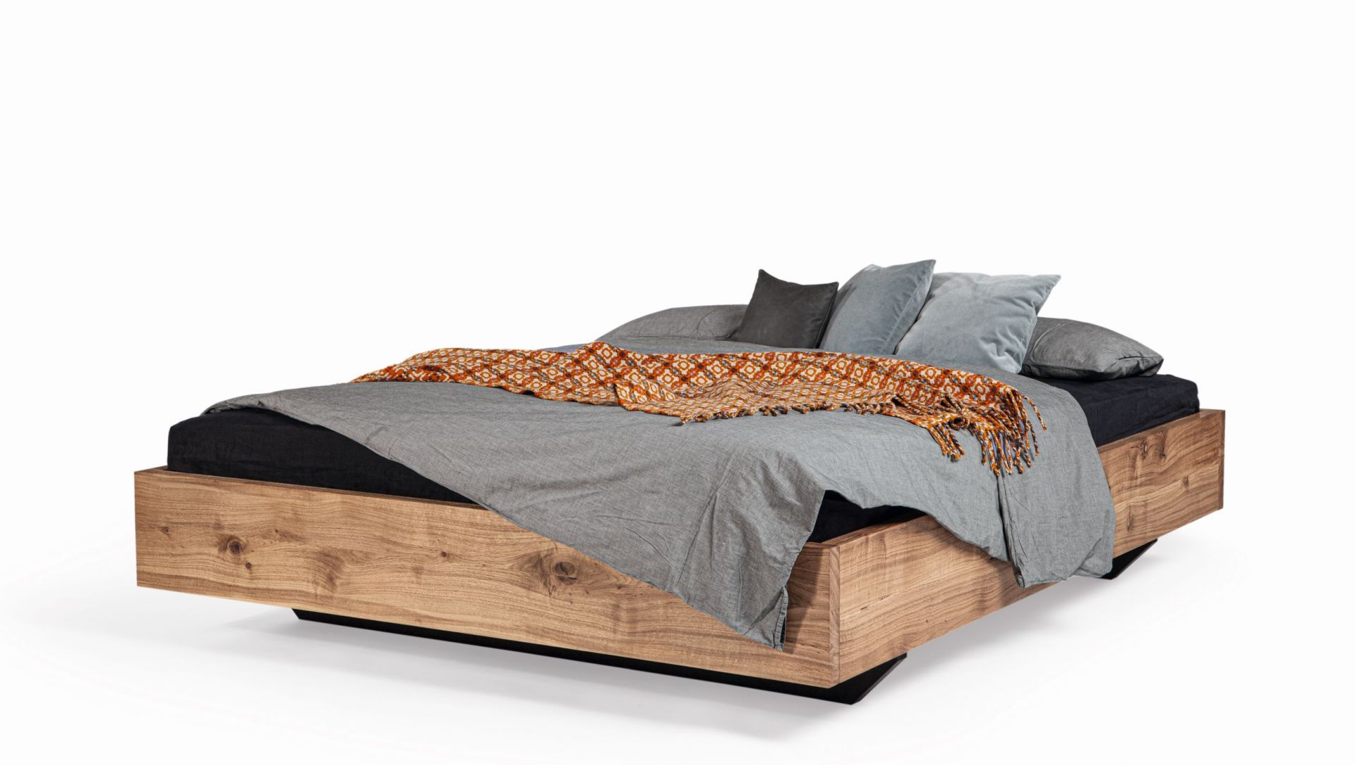 SC 56 Bett Janua: Modernes Holzbett mit grauer Bettwäsche und gemusterter Tagesdecke.