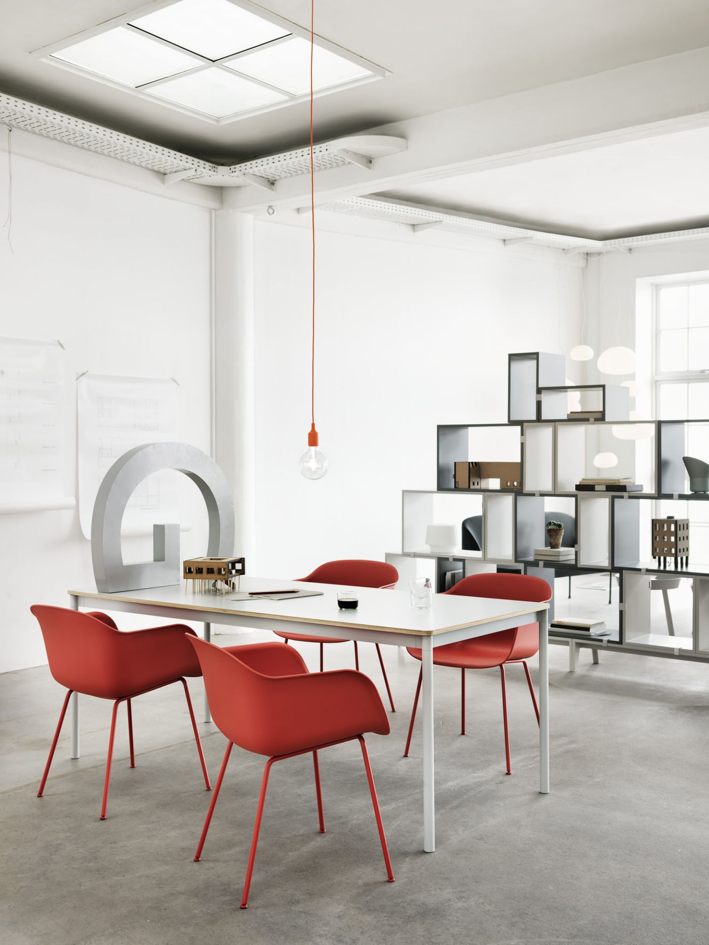 Heller Konferenzraum mit Muuto Base Table Tisch, roten Stühlen und modernem Regal im Hintergrund.
