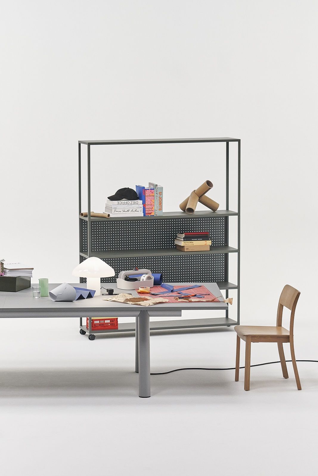 Heller Raum mit Boa Table Konferenztisch von Hay, grau, mit Büromaterialien und Regal im Hintergrund.