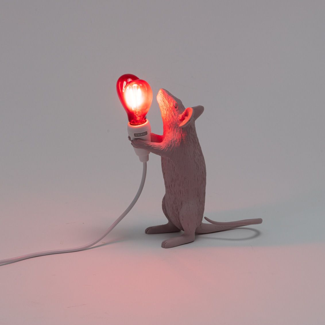 Seletti Mouse Lamp Step Love Edition: Graue Maus hält eine rote Herz-Glühbirne als Tischleuchte.