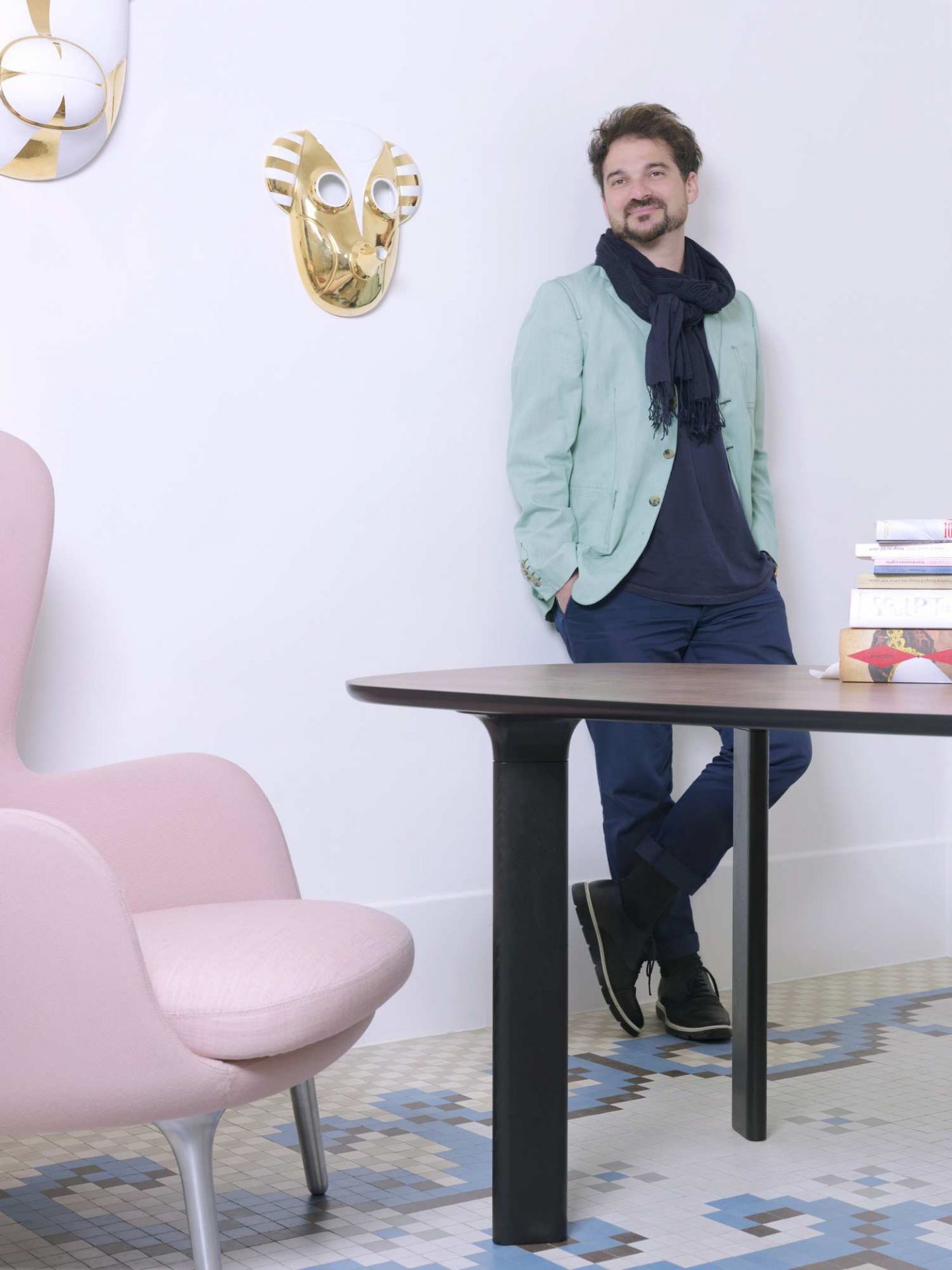 Mann lehnt an Fritz Hansen Analog Tisch mit rosa Sessel und goldener Wanddekoration im Hintergrund.