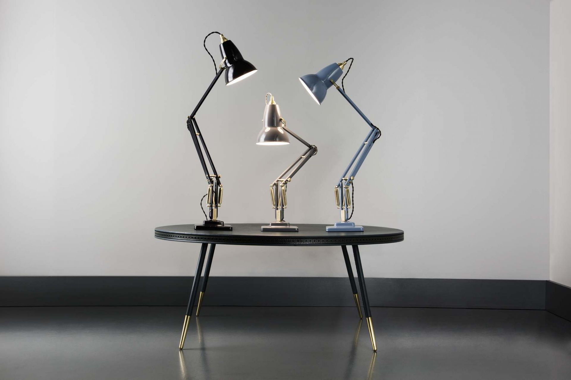 Drei Anglepoise Original 1227 Messing Tischleuchten in Schwarz, Silber und Blau auf einem Tisch.