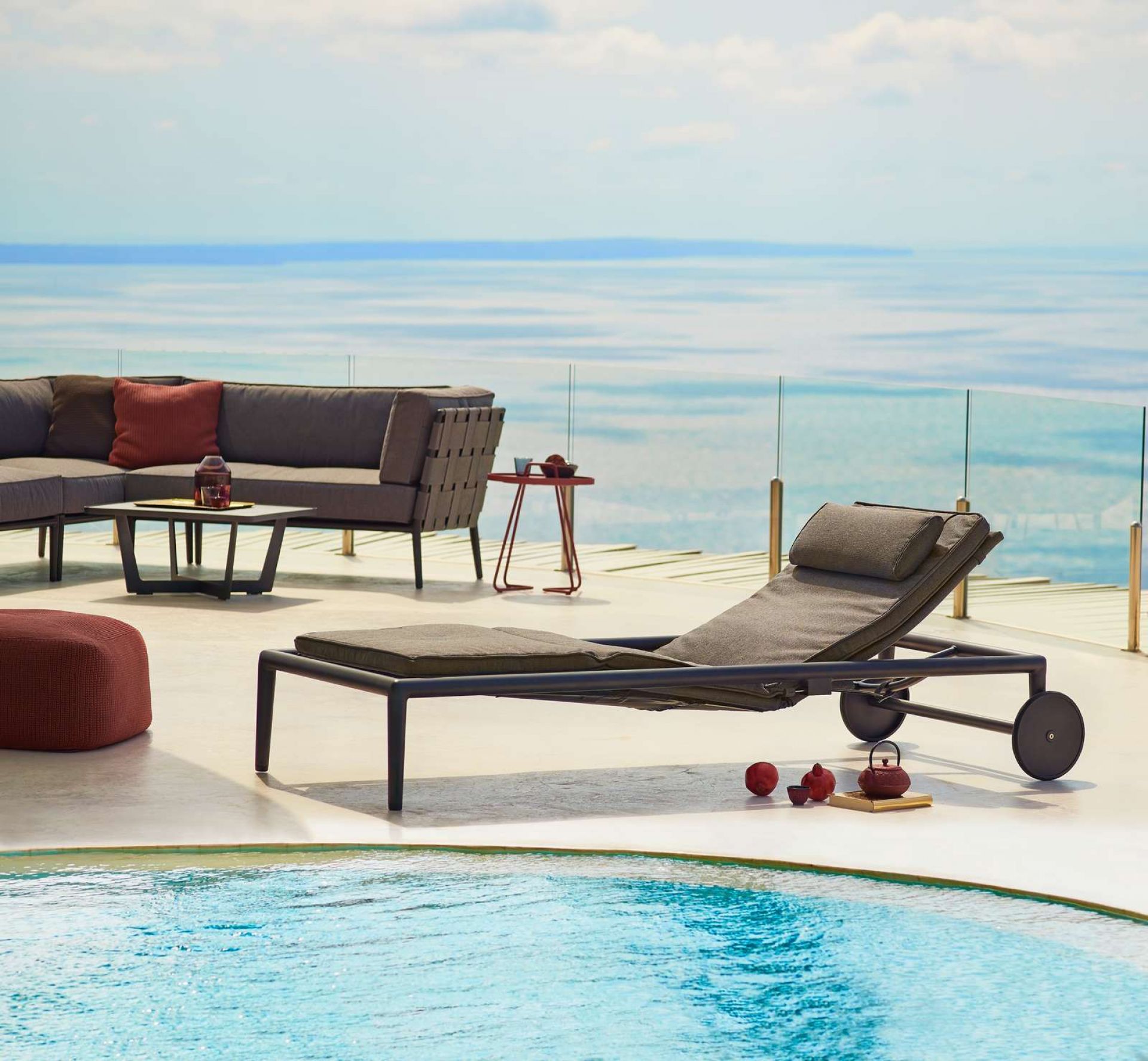 Cane-Line Conic Sonnenliege im Outdoor-Bereich mit Pool und Meerblick. Moderne Gartenliege mit Rädern.