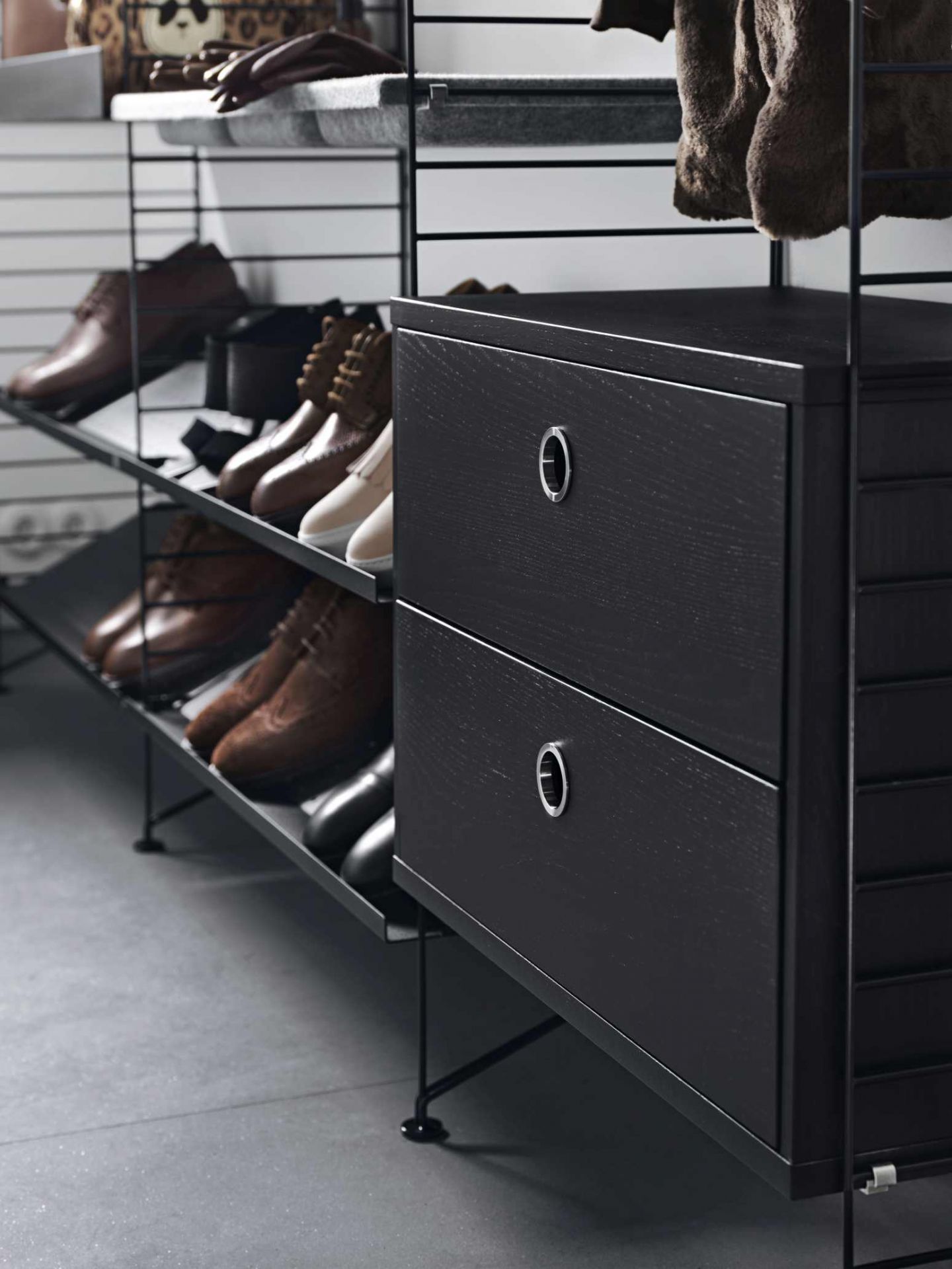 Schwarzer String Nachttisch mit zwei Schubladen und Schuhregalen im modernen Schlafzimmer.