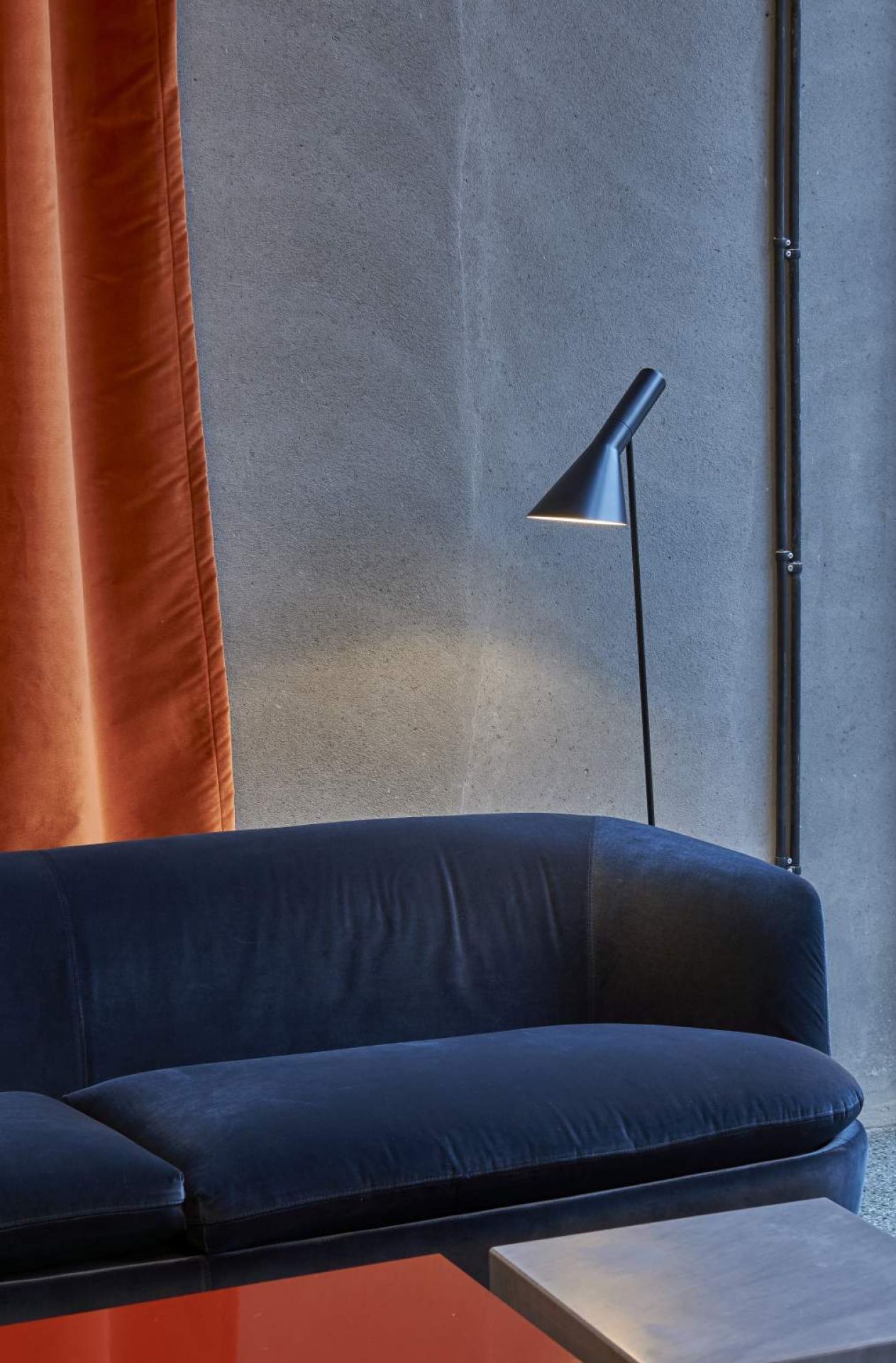 AJ Stehleuchte in Blass Petroleum von Louis Poulsen neben einem blauen Sofa und Vorhang.