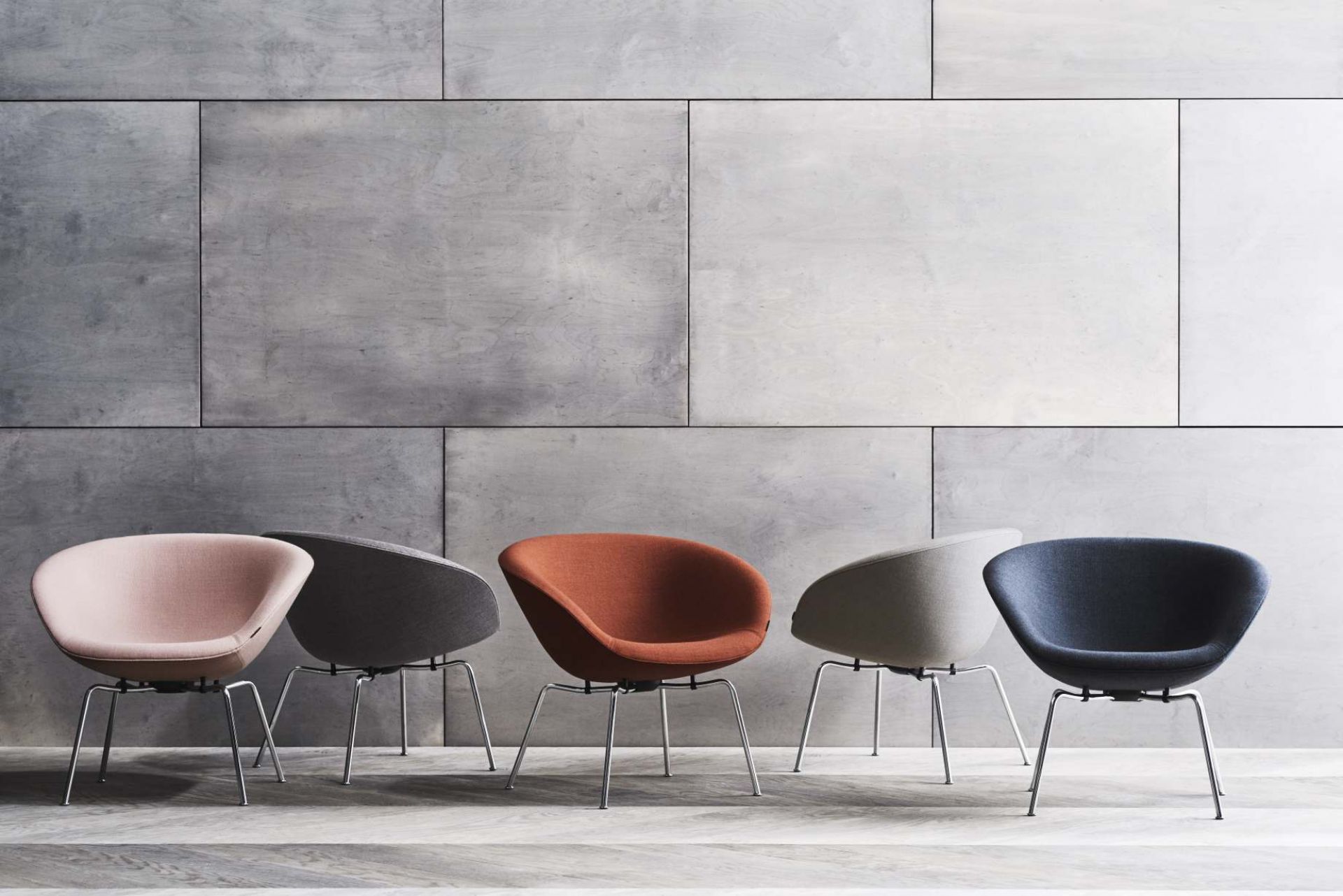 Fünf Fritz Hansen Pot Sessel in verschiedenen Farben vor einer grauen Wand.