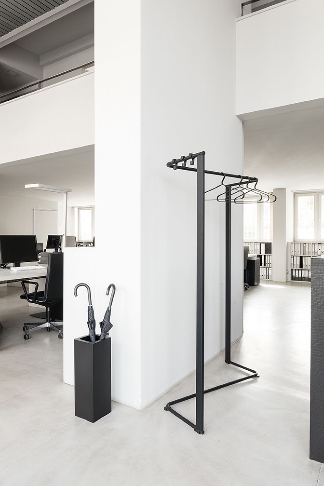 Schwarzer Schönbuch Kleiderbügel "Angle" im minimalistischen Design mit Kleiderbügeln und Schirmständer in modernem Büro.