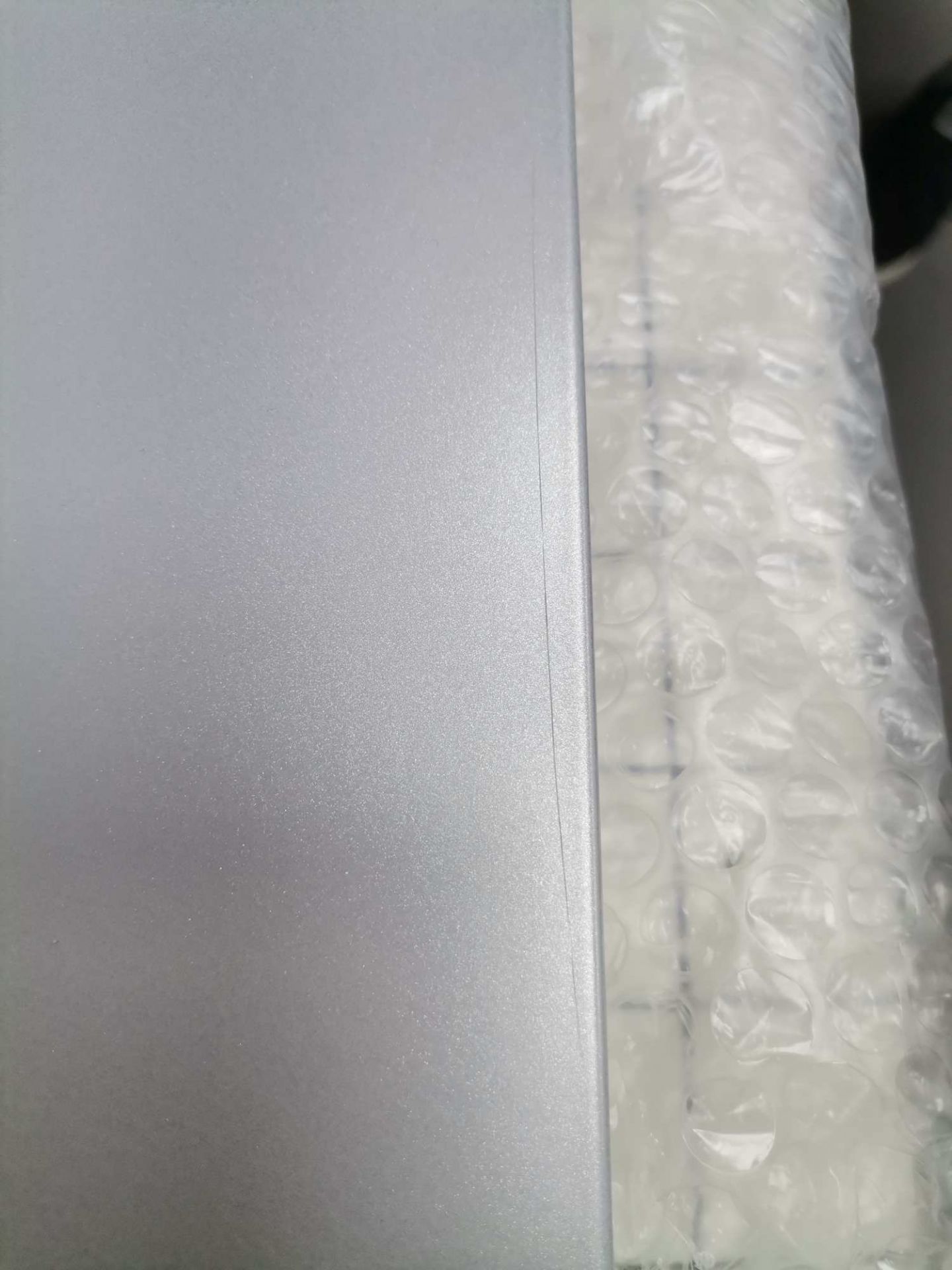 Detailaufnahme eines silbernen USM Haller Ersatzteils, verpackt in Luftpolsterfolie, Mängelexemplar.
