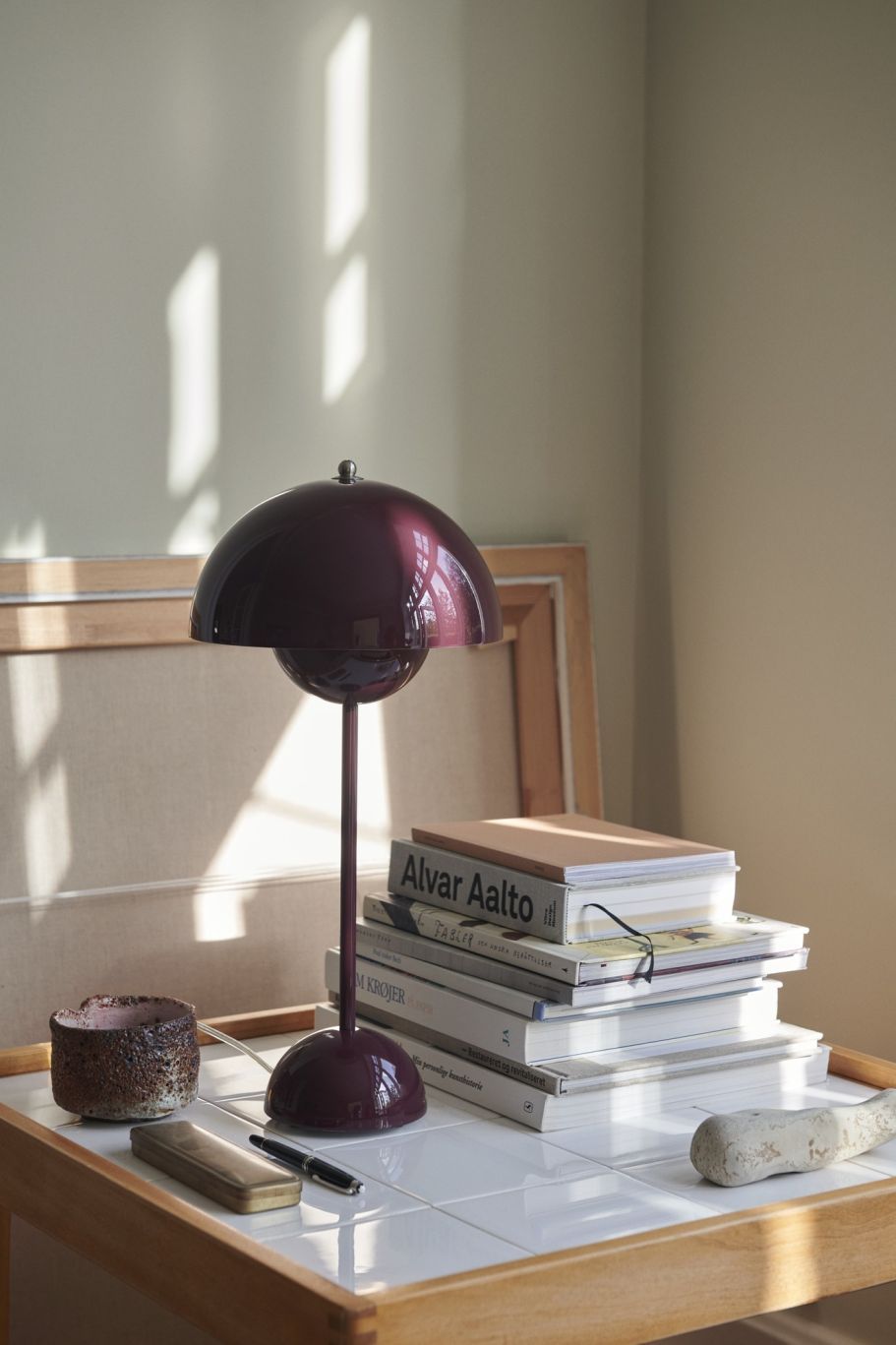 Nahaufnahme der AndTradition Flowerpot VP3 Tischleuchte in Aubergine, platziert auf einem Tisch mit Büchern und Dekoration.