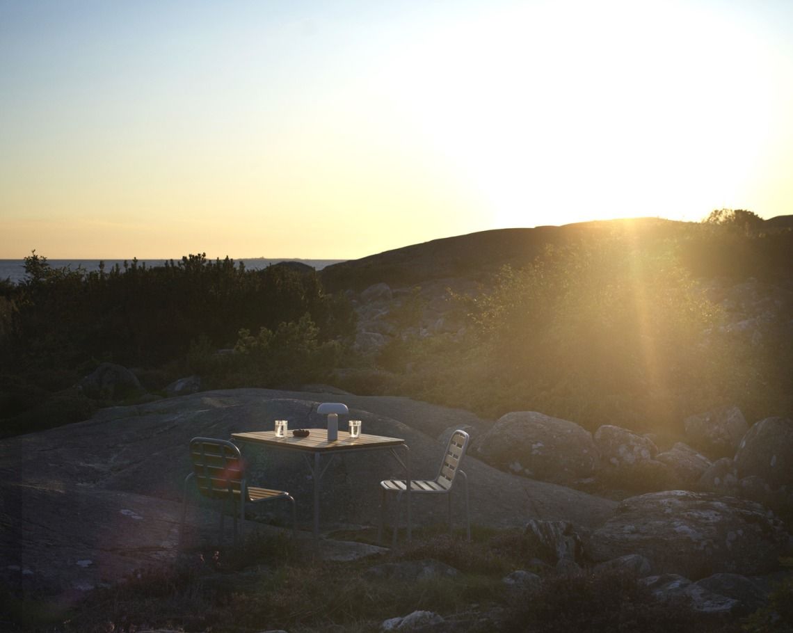 Normann Copenhagen Vig Table Outdoor mit Stühlen und Getränken bei Sonnenuntergang.