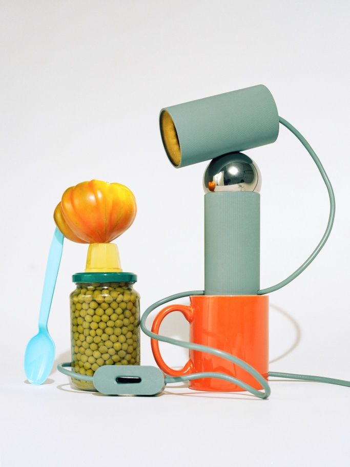 Verspielte Bilboquet Tischleuchte: Stillleben mit Lampe, Konservenglas, Tasse und Löffel vor weißem Hintergrund.