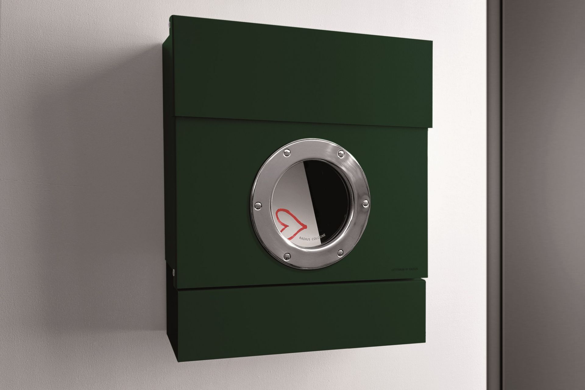 Dunkelgrüner Letterman II Radius Briefkasten mit Bullauge an einer weißen Wand, moderne Hauspostanlage.