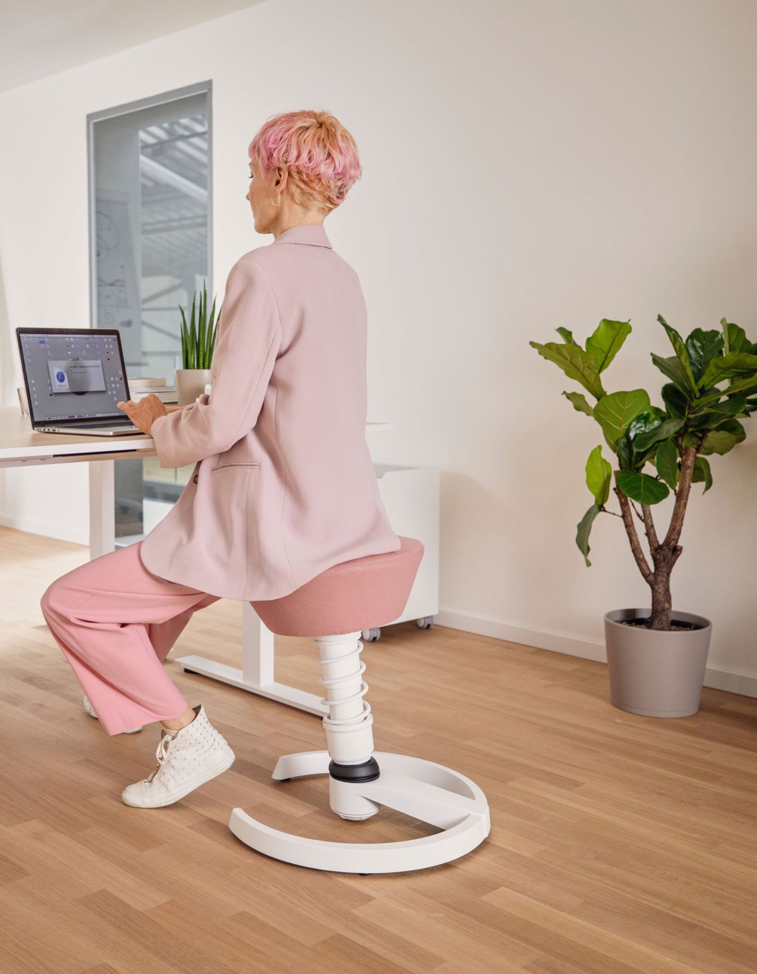 Frau sitzt auf einem rosa Swopper Hocker von Aeris vor einem Laptop.