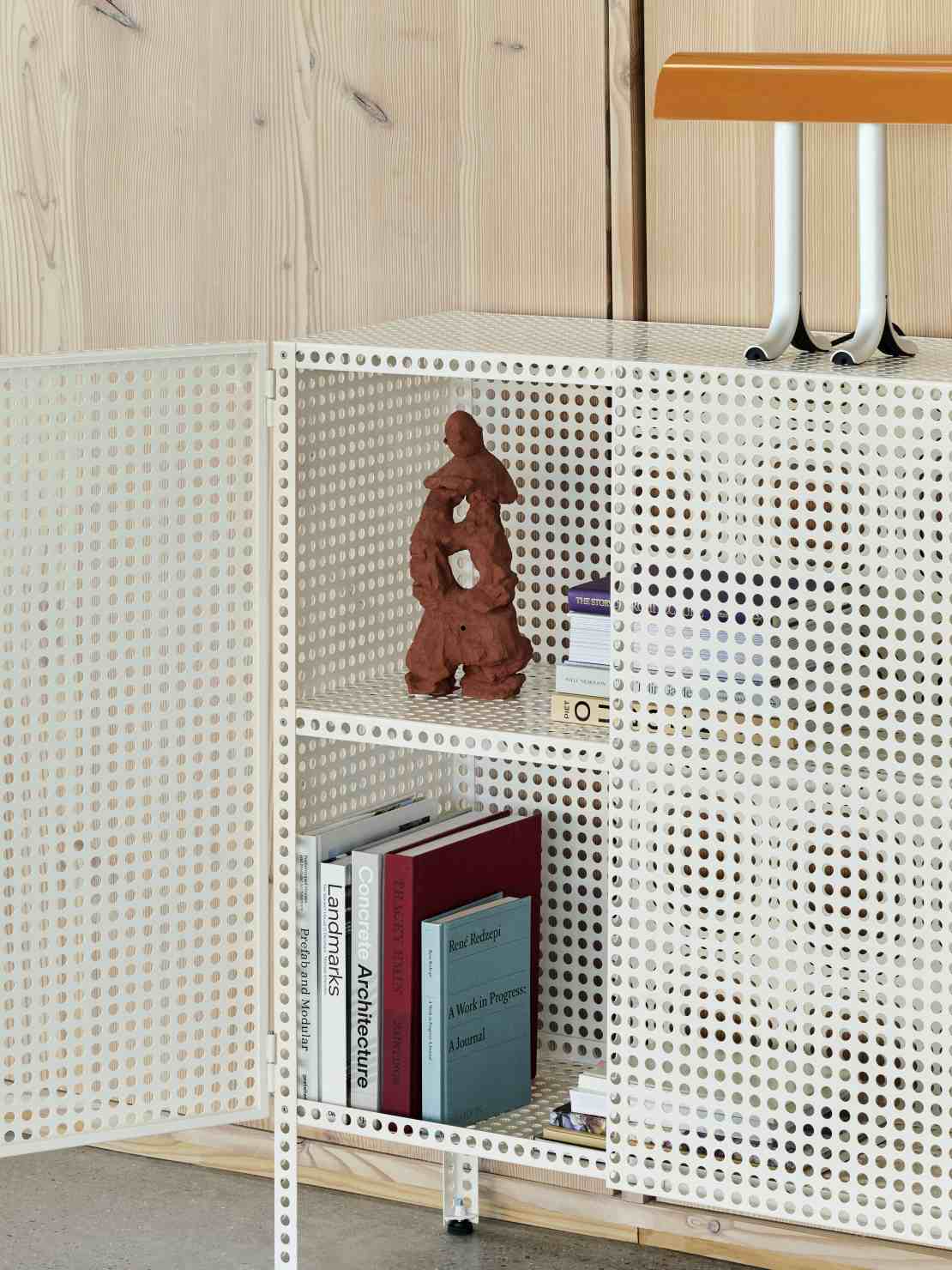 Weißes Hay Sideboard "Perforated Cabinet Floor Medium" mit perforierter Metallstruktur, Büchern und Dekoration.