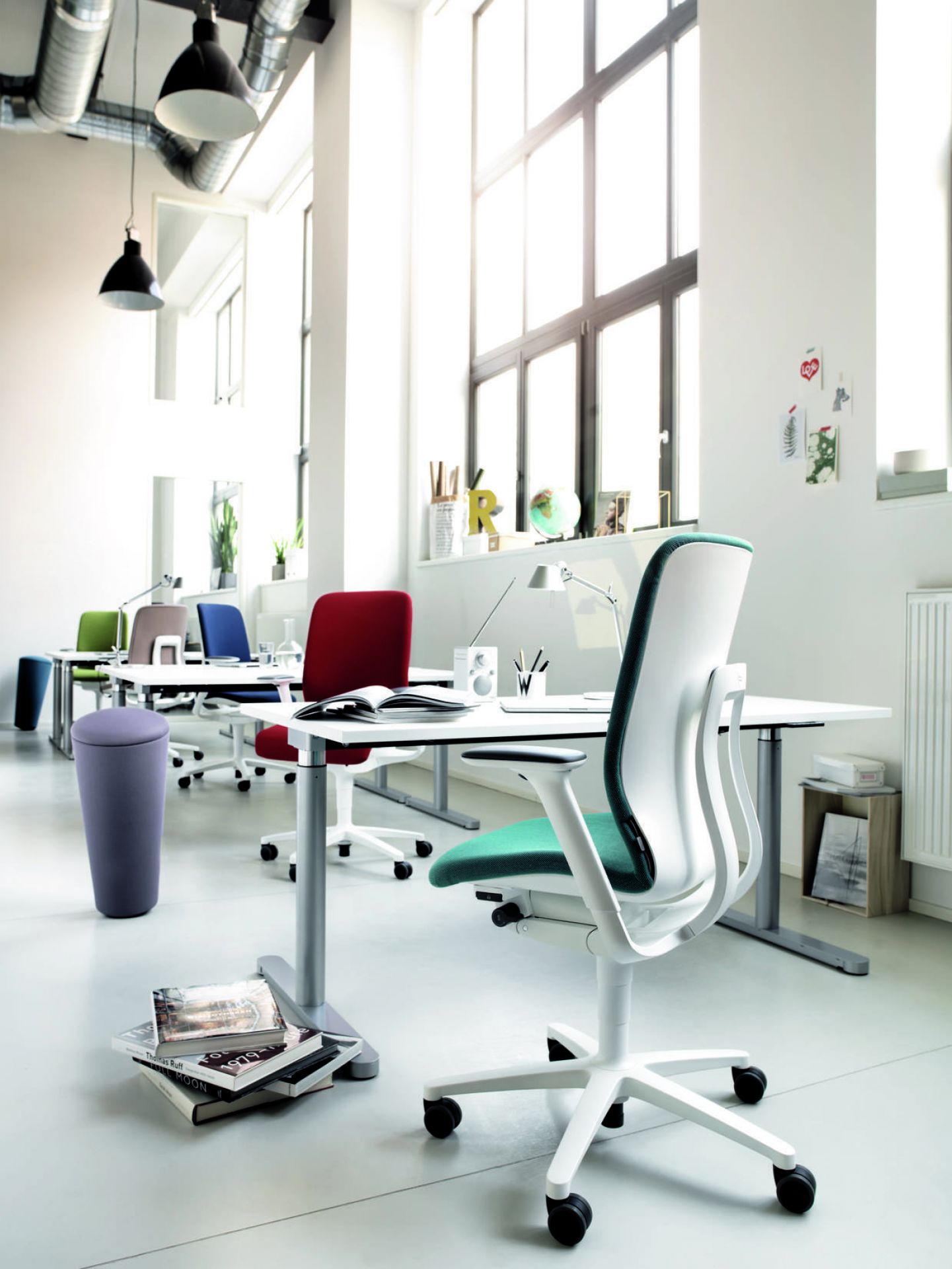 Moderner Büroraum mit ergonomischem Bürostuhl in Weiß und Türkis, höhenverstellbaren Schreibtischen und stylischem Hocker.