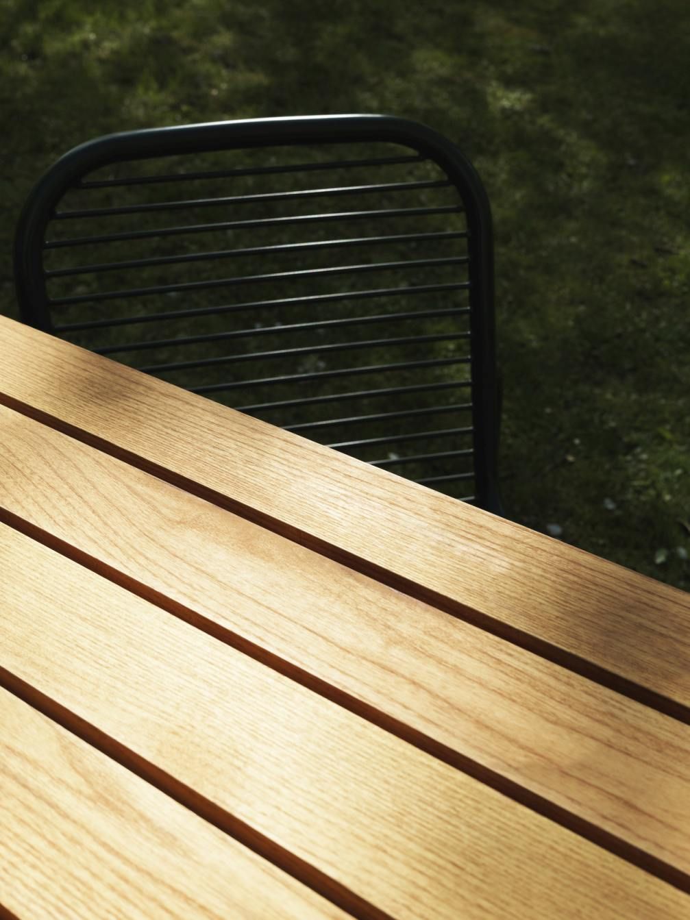 Detailaufnahme des Normann Copenhagen Vig Tisch Outdoor mit Holzoberfläche und einem Stuhl im Hintergrund.