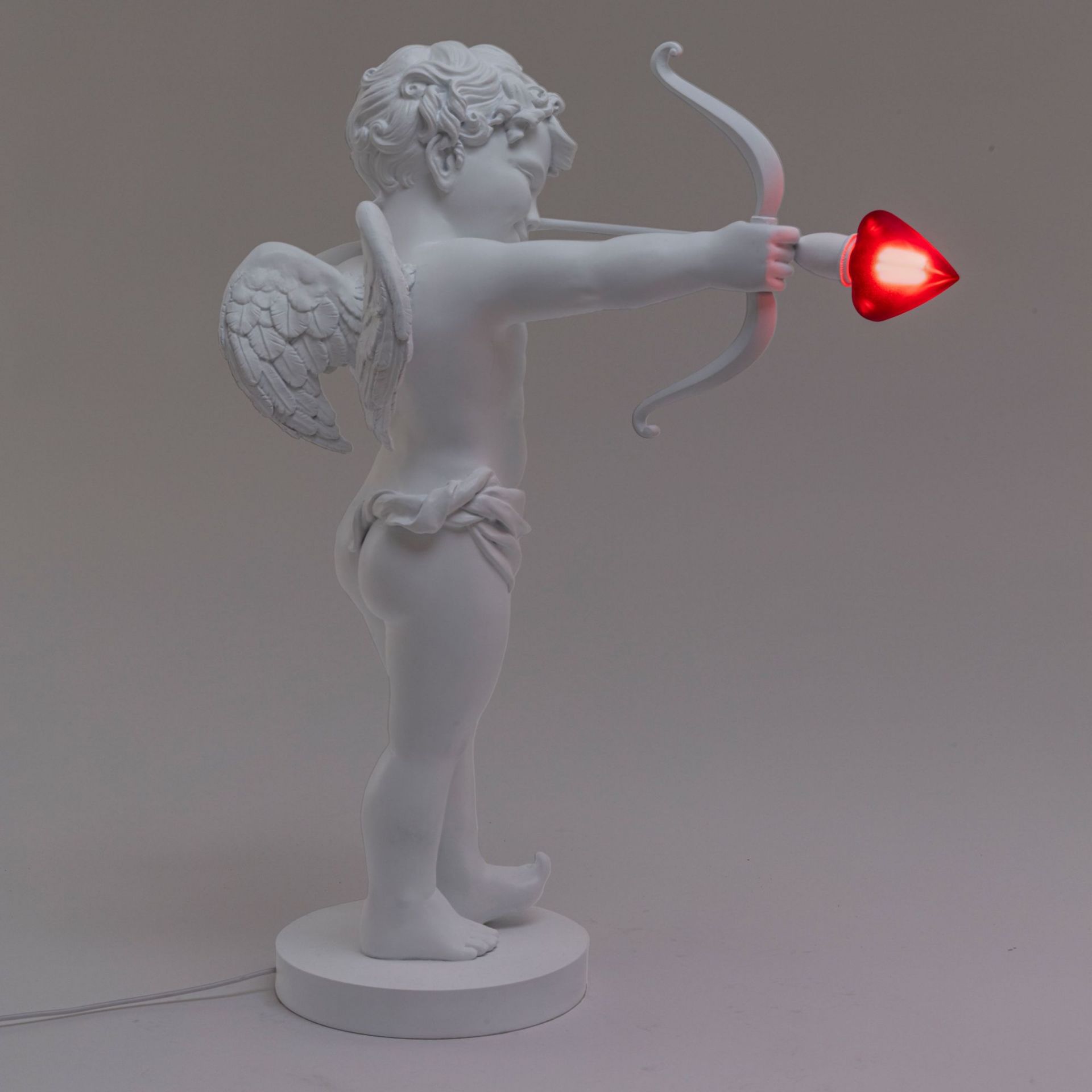Cupid Lampe von Seletti, weiße Amor Statue mit Bogen und rotem Herz als Leuchtmittel.