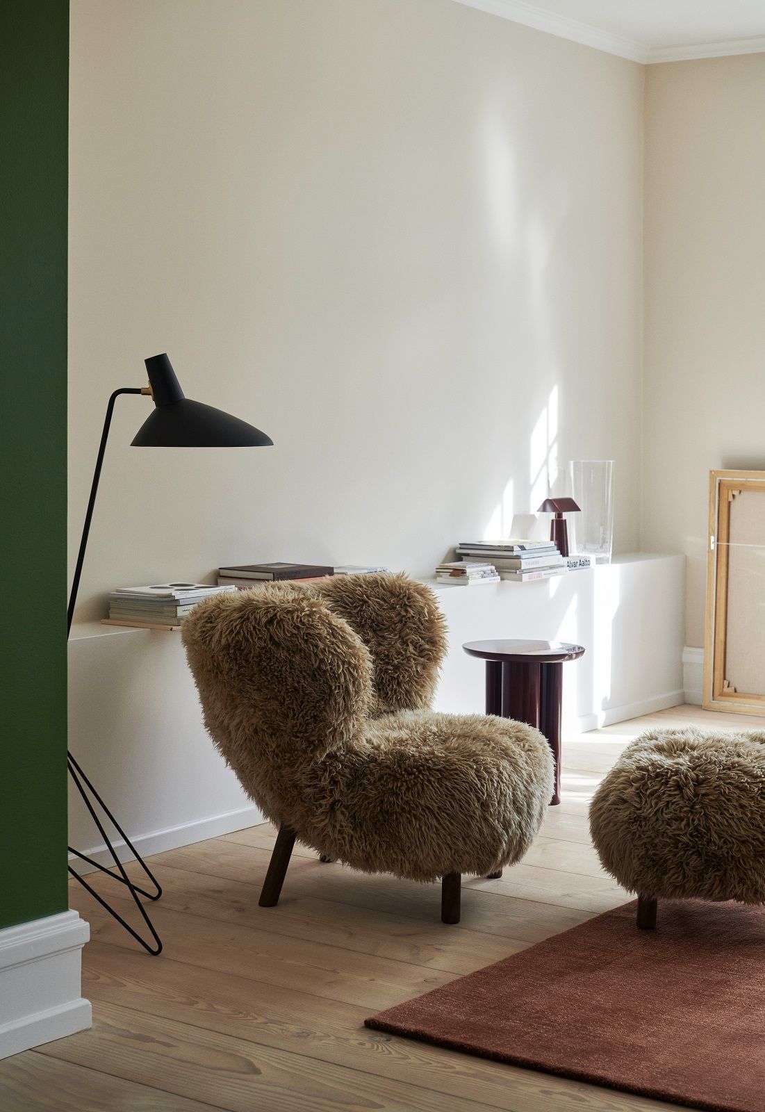AndTradition Tripod HM8 Stehleuchte in Schwarz neben Sessel und Beistelltisch im Wohnzimmer.