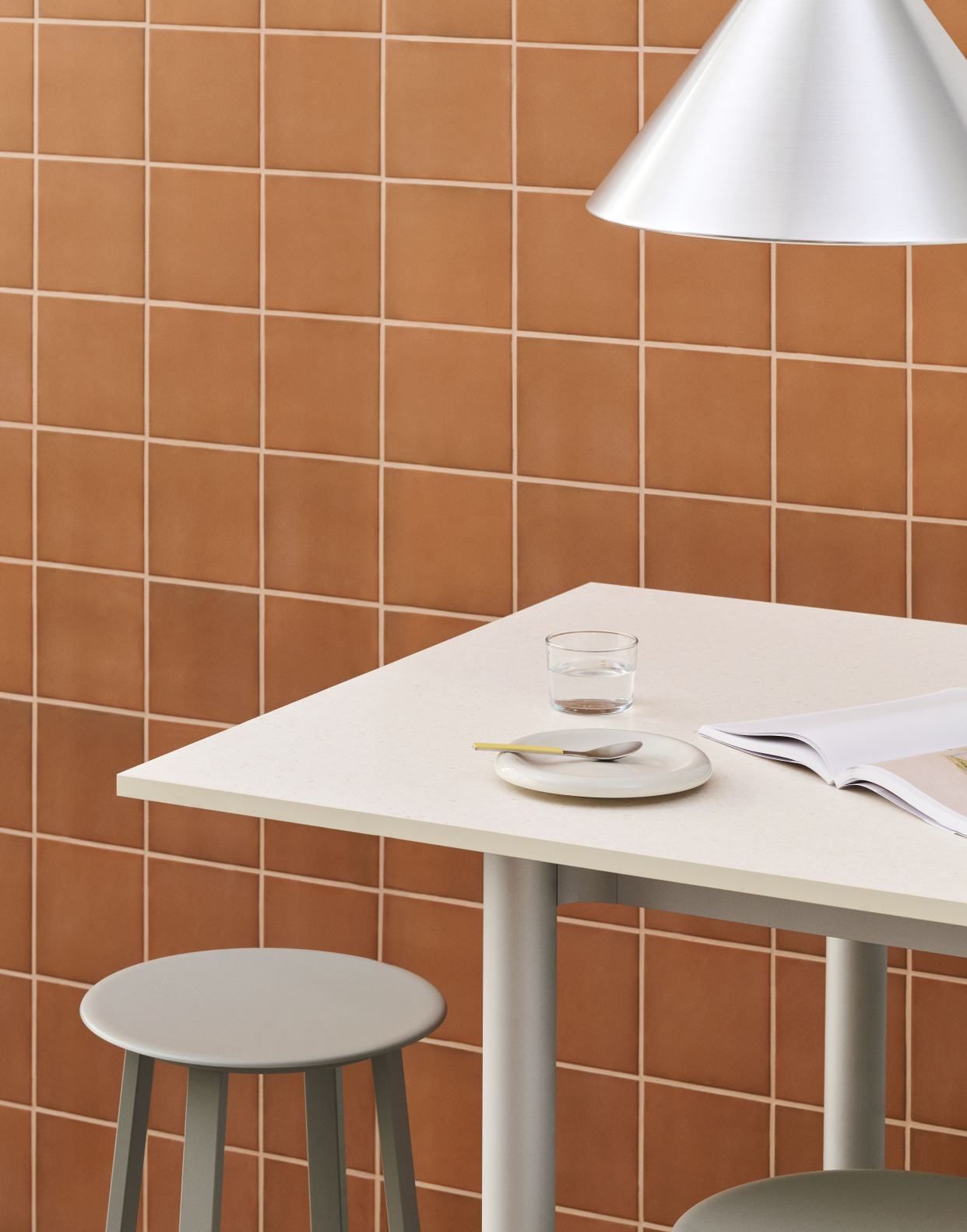 Annex Table Overhang Esstisch von Hay mit Stühlen, Geschirr und Magazin vor brauner Kachelwand.