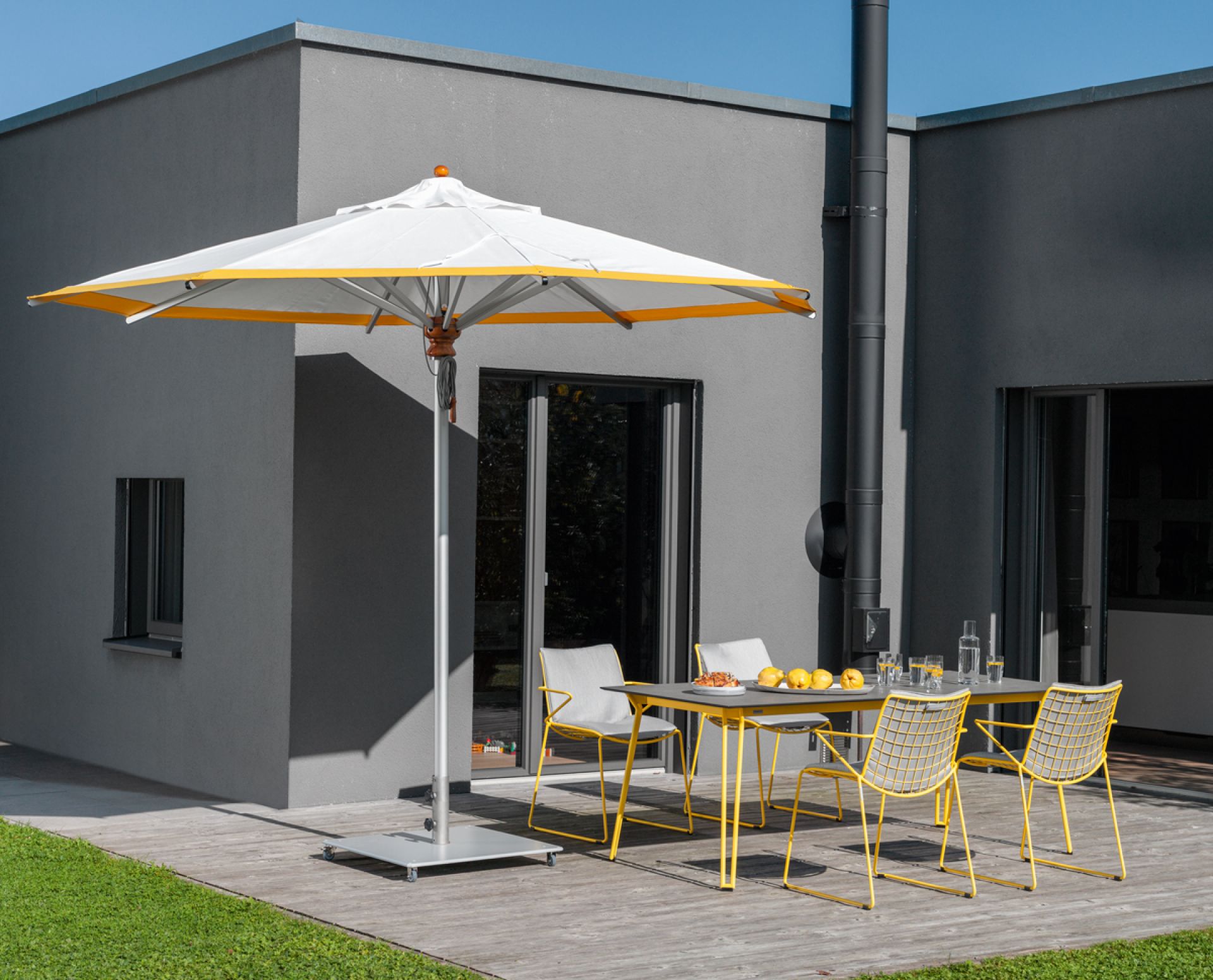 Alusonnenschirm rund grau von Weishäupl spendet Schatten auf einer Terrasse mit Gartenmöbeln.