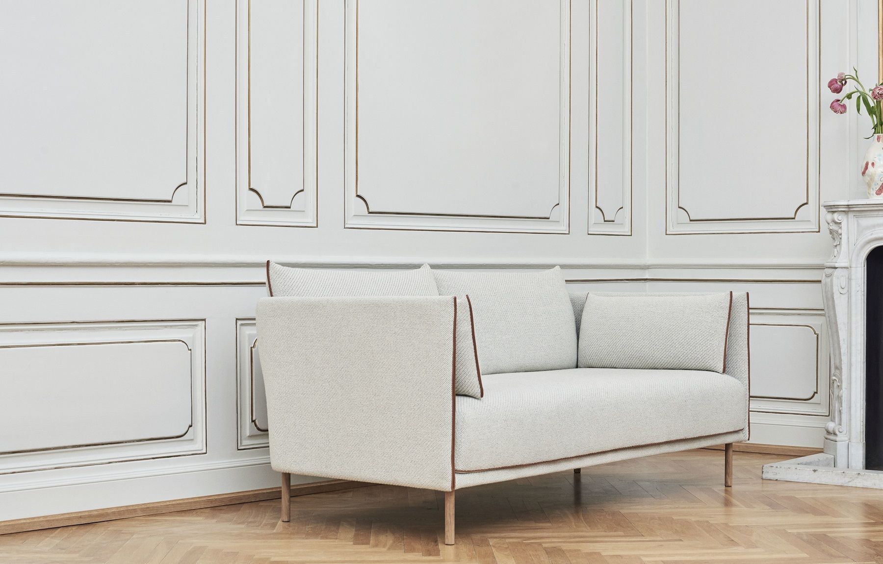 Silhouette Sofa 2-Sitzer Low Hay, hellgraues modernes Sofa mit braunen Akzenten vor weißer Wand.