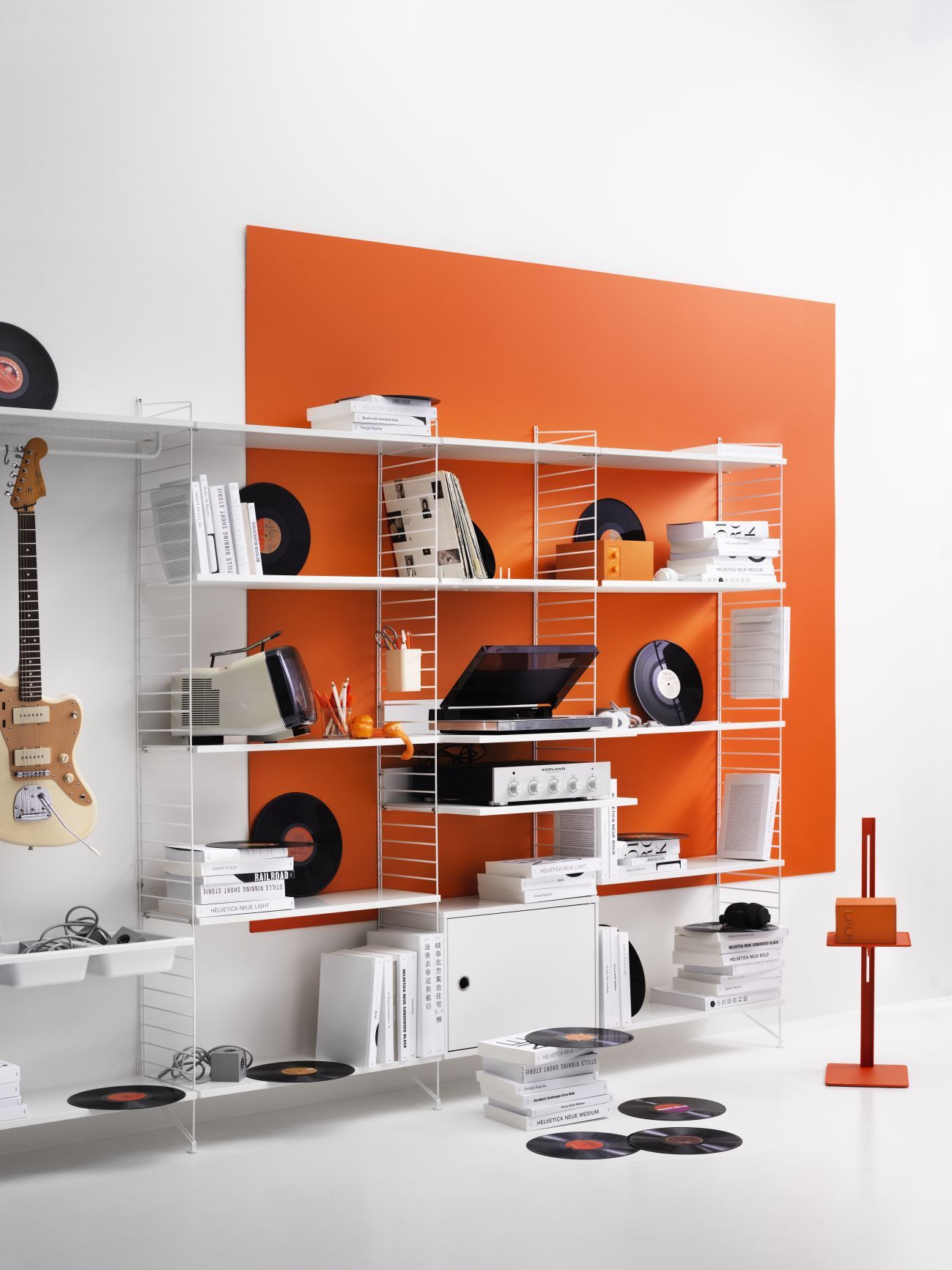 Beiges String Regalsystem an der Wand, gefüllt mit Büchern, Schallplatten und Elektronik. Wohnzimmer Einrichtung.