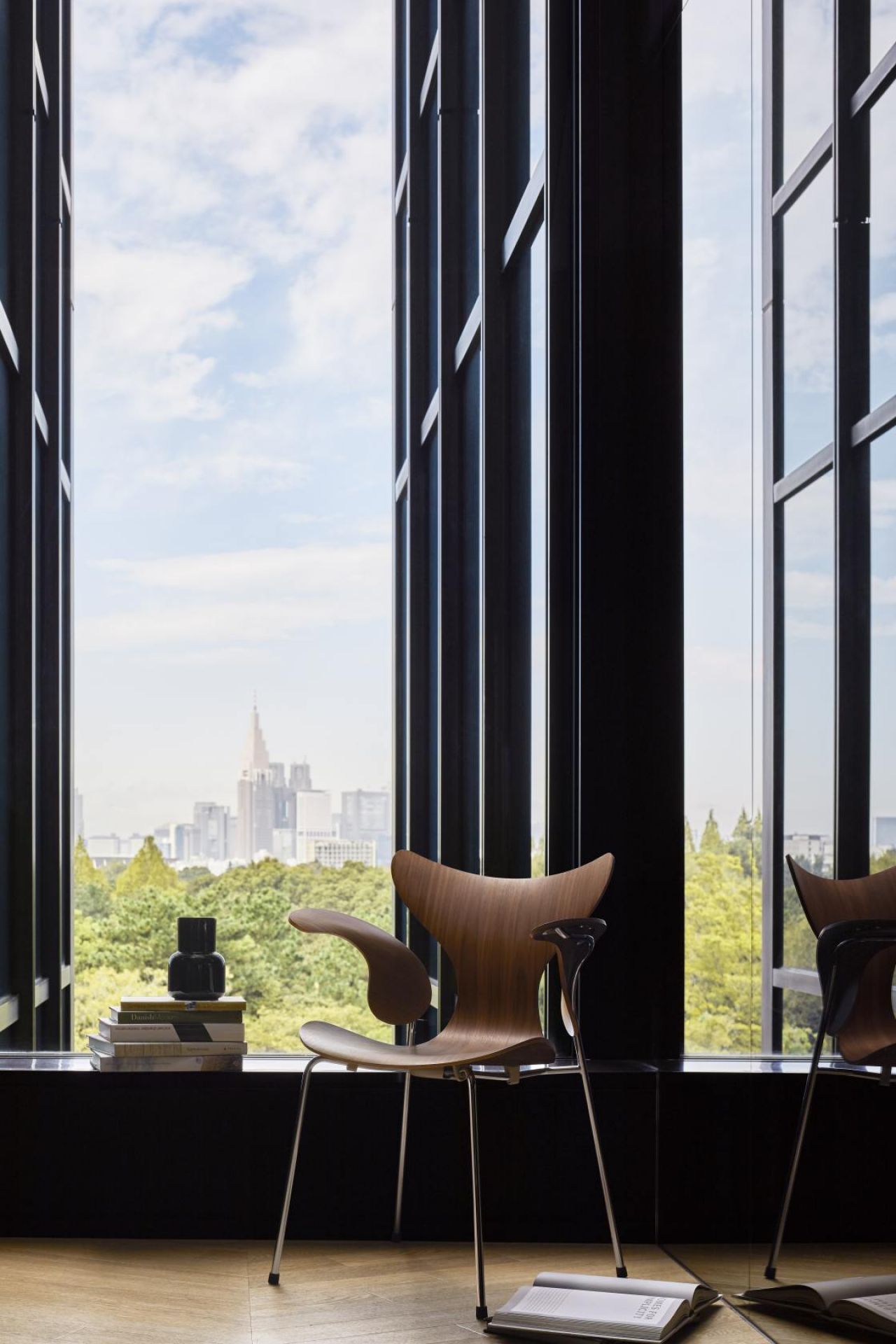 Fritz Hansen Lily Armlehnenstuhl 3208 aus Holz mit Stahlbeinen vor Fenster mit Stadtblick.