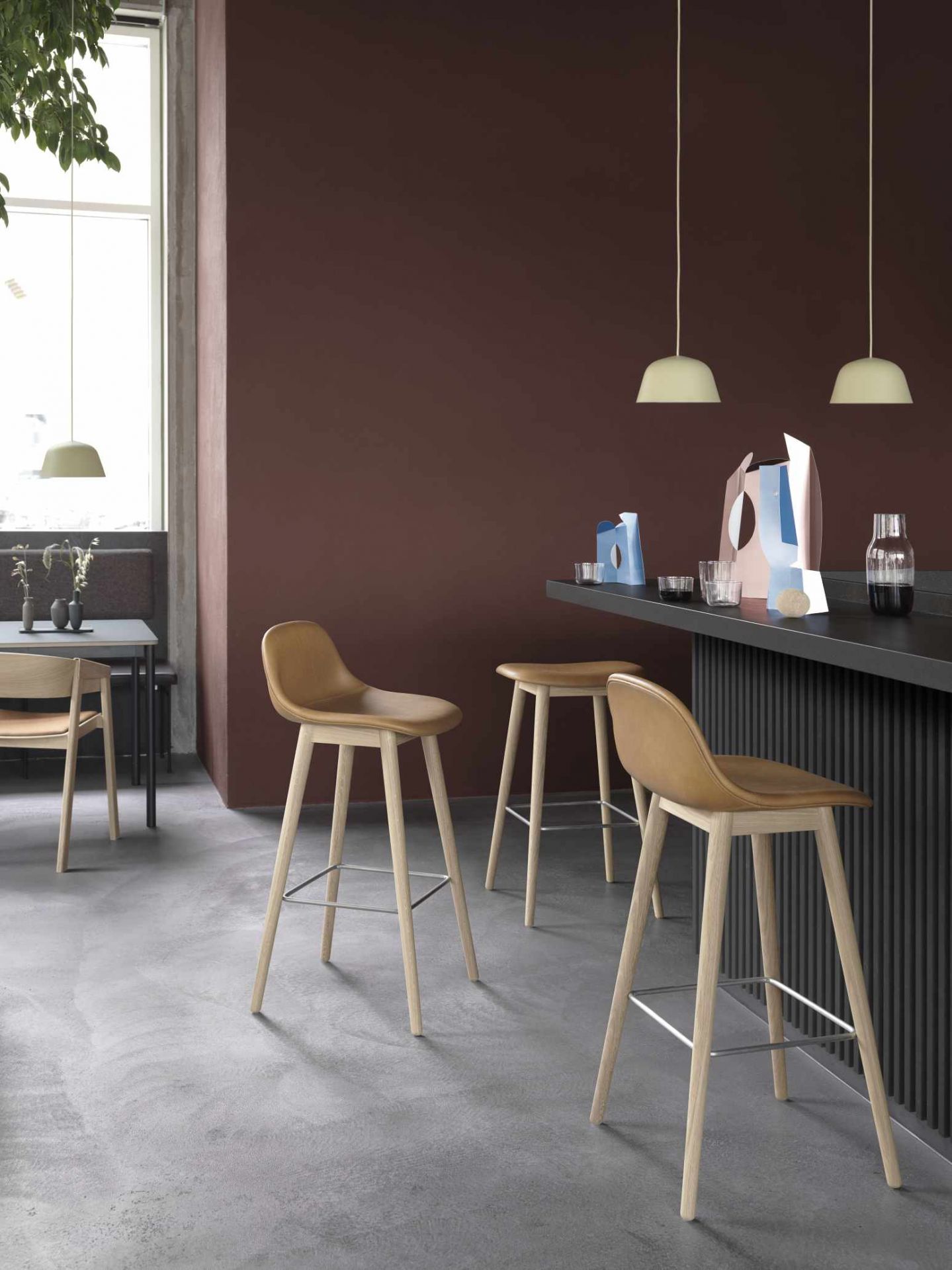 Helle Ambit Pendelleuchten von Muuto über Barhockern in modernem Interieur mit brauner Wand.