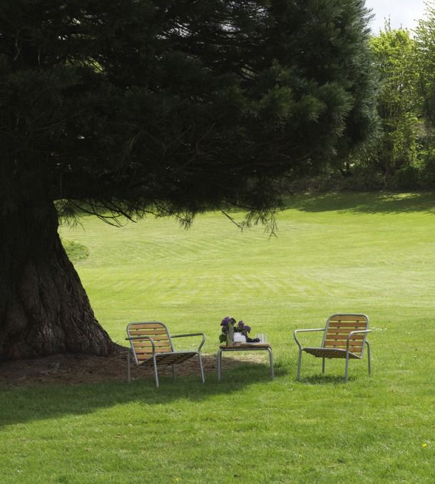 Normann Copenhagen Vig Table Outdoor mit zwei Stühlen auf einer grünen Wiese unter einem Baum.