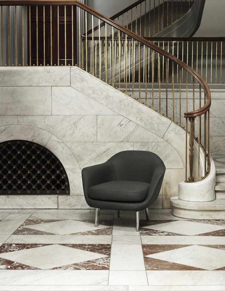Dunkelgrauer Sum Lounge Armchair Sessel von Normann Copenhagen vor Marmorwand mit Treppe und goldenem Geländer.