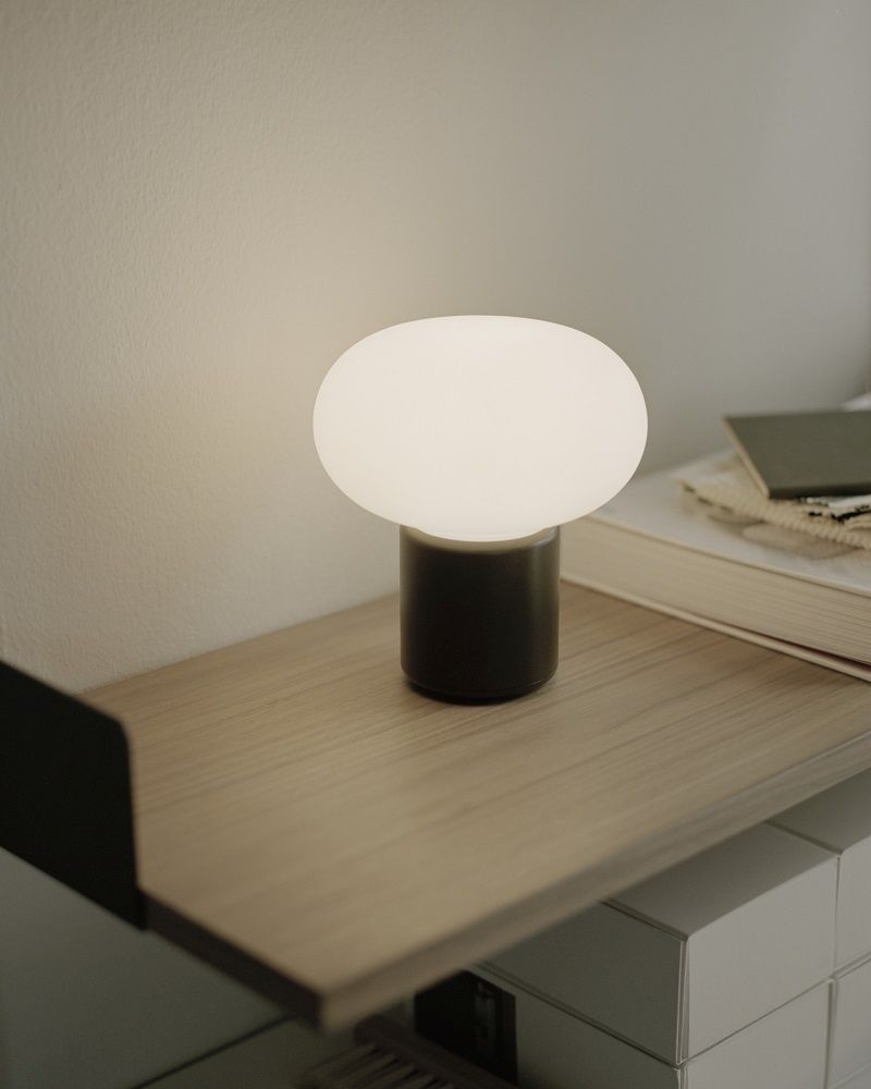 New Works Karl-Johan Tischleuchte: Akkuleuchte mit ovalem Lampenschirm auf einem Nachttisch.