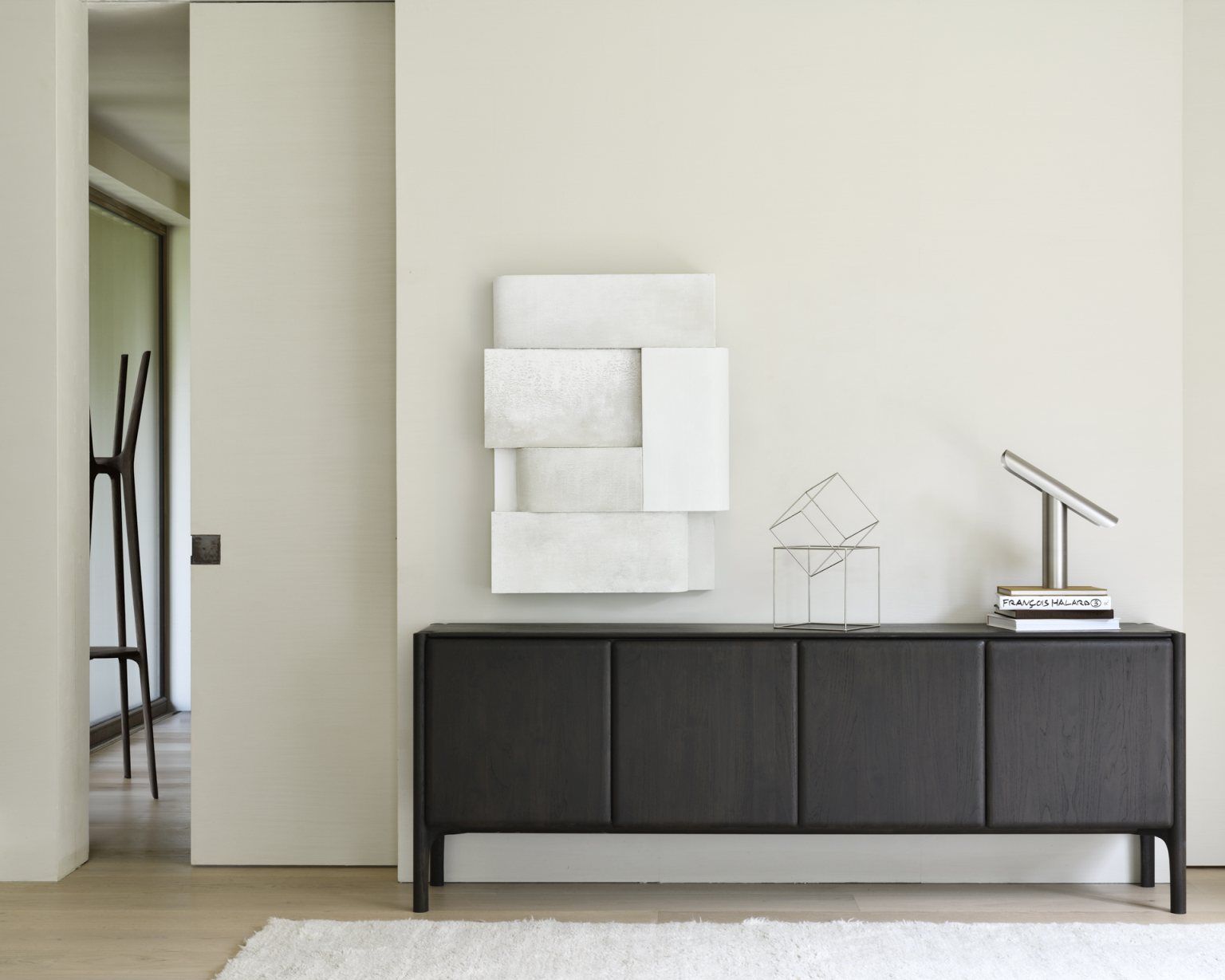 Ethnicraft Sideboard aus dunklem Holz mit minimalistischer Dekoration und weißem Teppich im modernen Wohnzimmer.