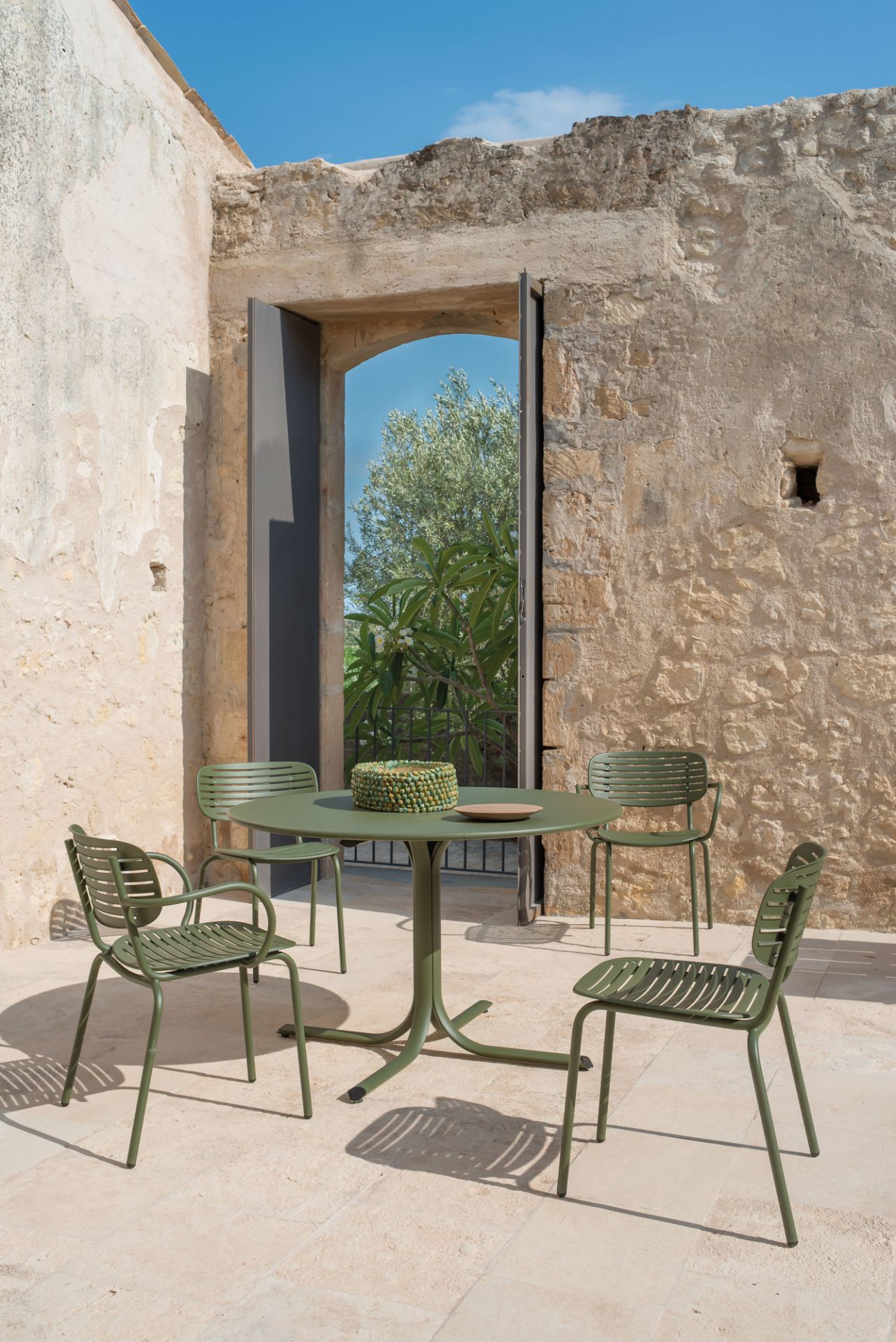 Grüne Emu Mom Stühle und runder Gartentisch aus Metall auf einer Terrasse mit Steinmauer.