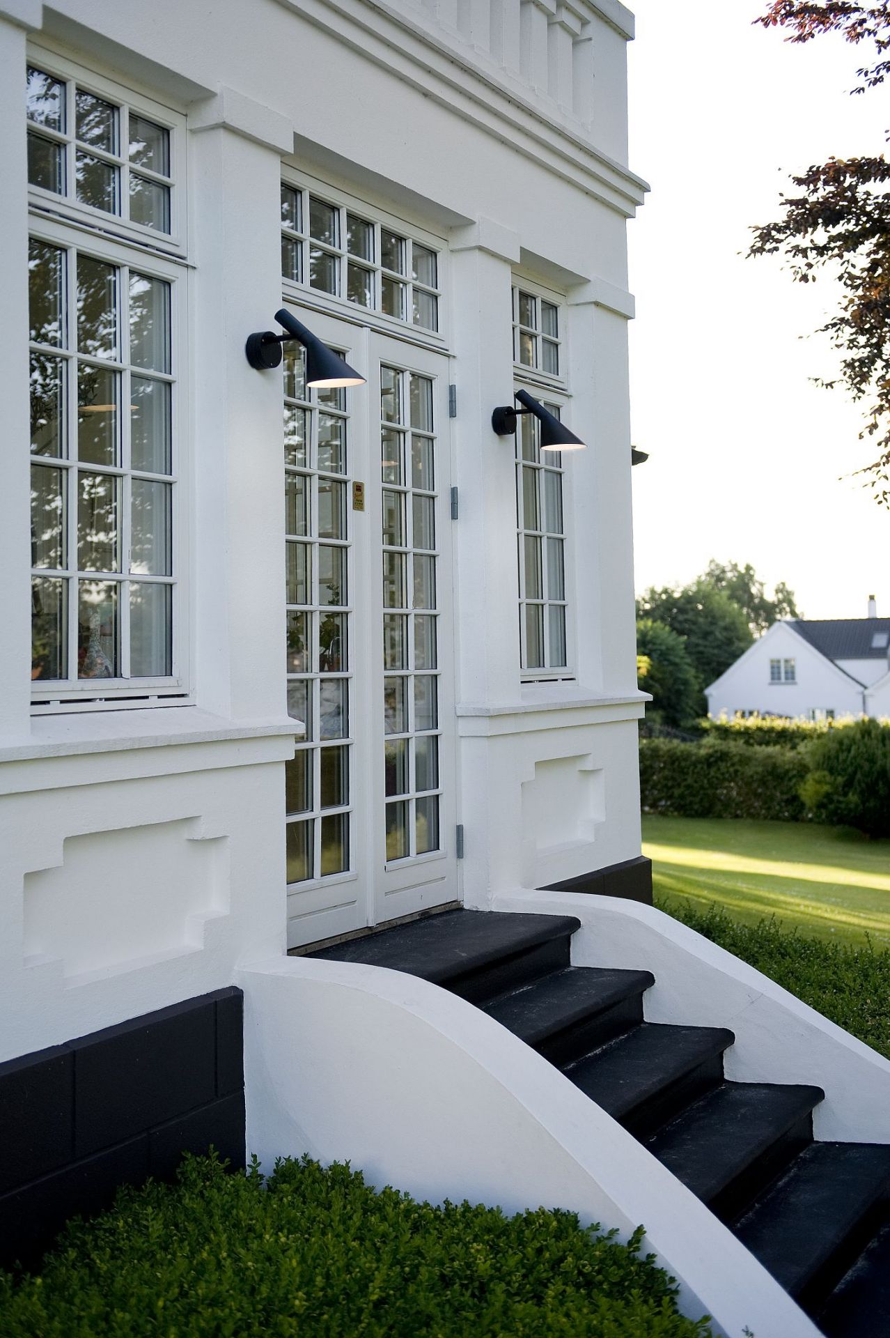 Nahaufnahme einer weißen Hausfassade mit zwei AJ 50 Wandleuchten von Louis Poulsen.