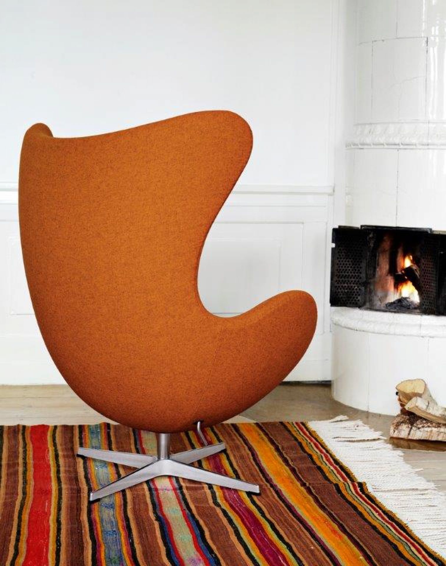 Orangefarbener Egg Chair Sessel von Fritz Hansen mit Hocker auf einem bunten Teppich vor Kamin.