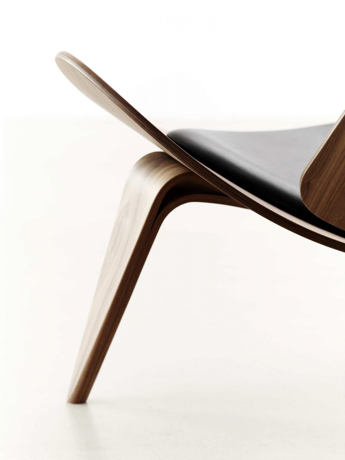 Detailaufnahme des CH07 Shell Chair Stuhls von Carl Hansen mit schwarzem Lederbezug und Holzgestell.
